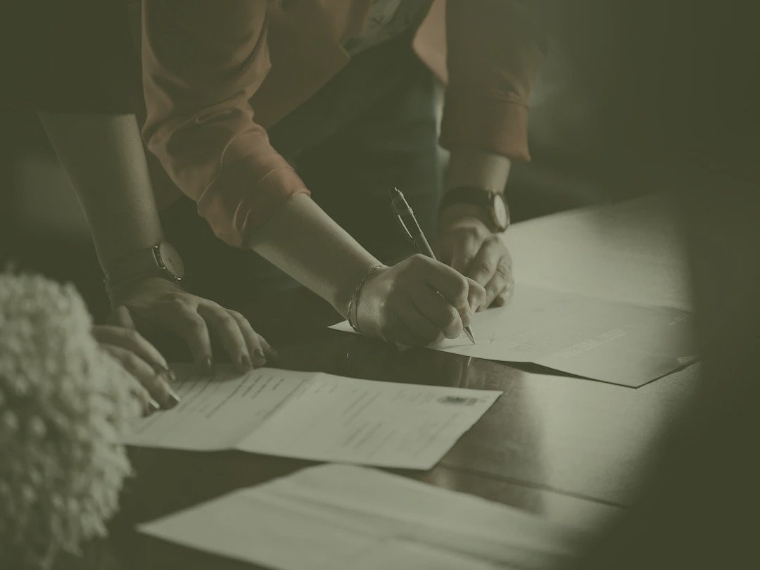 Person signing agreement documents at a wooden table
