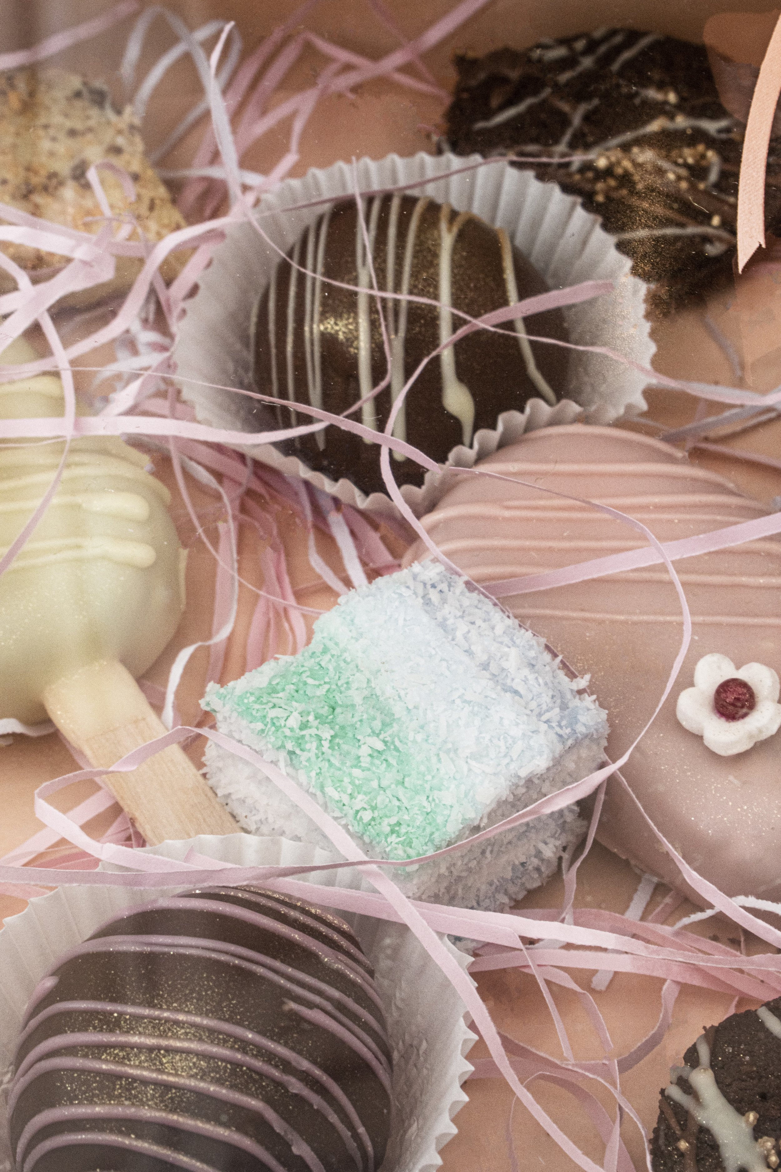 Assorted decorated chocolates and candies surrounded by pink paper shreds.