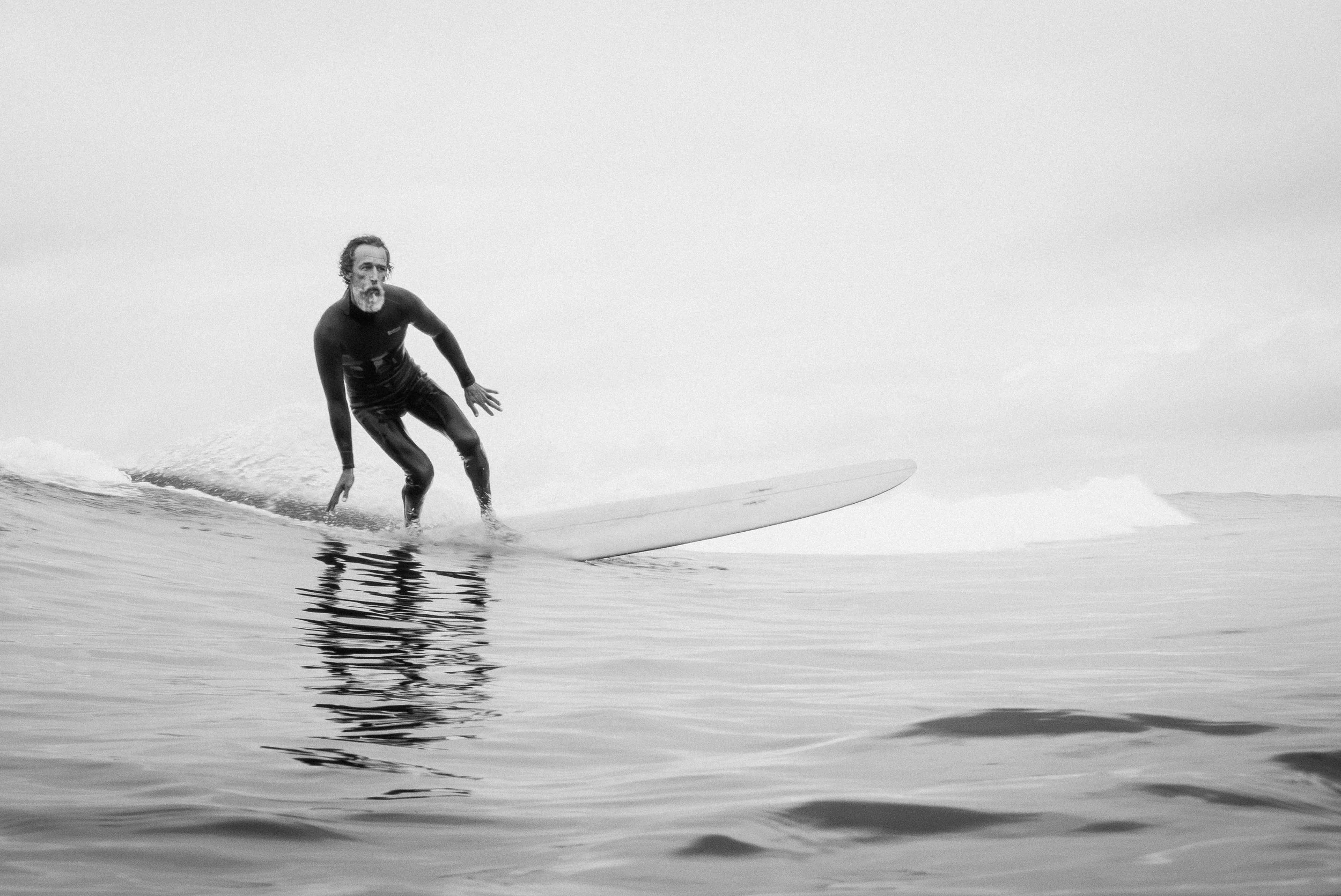 A black-and-white photograph of a man surfing on a calm ocean, with the sky and water blending into a minimalistic scene.