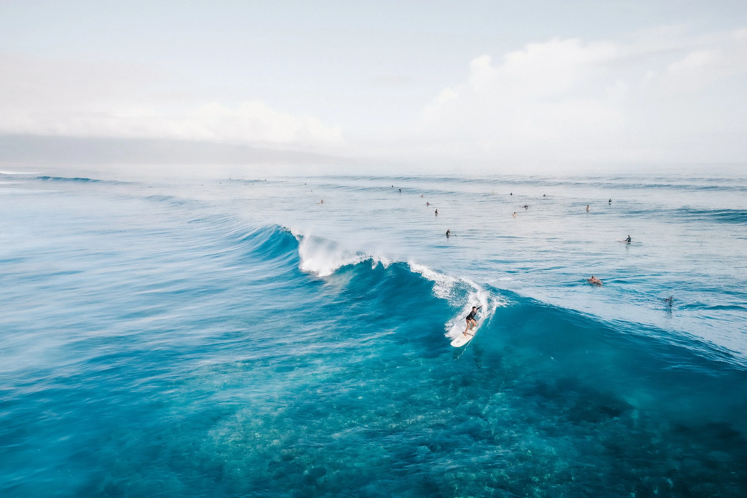 Surfer riding a wave in the ocean with many other surfers in the distance.