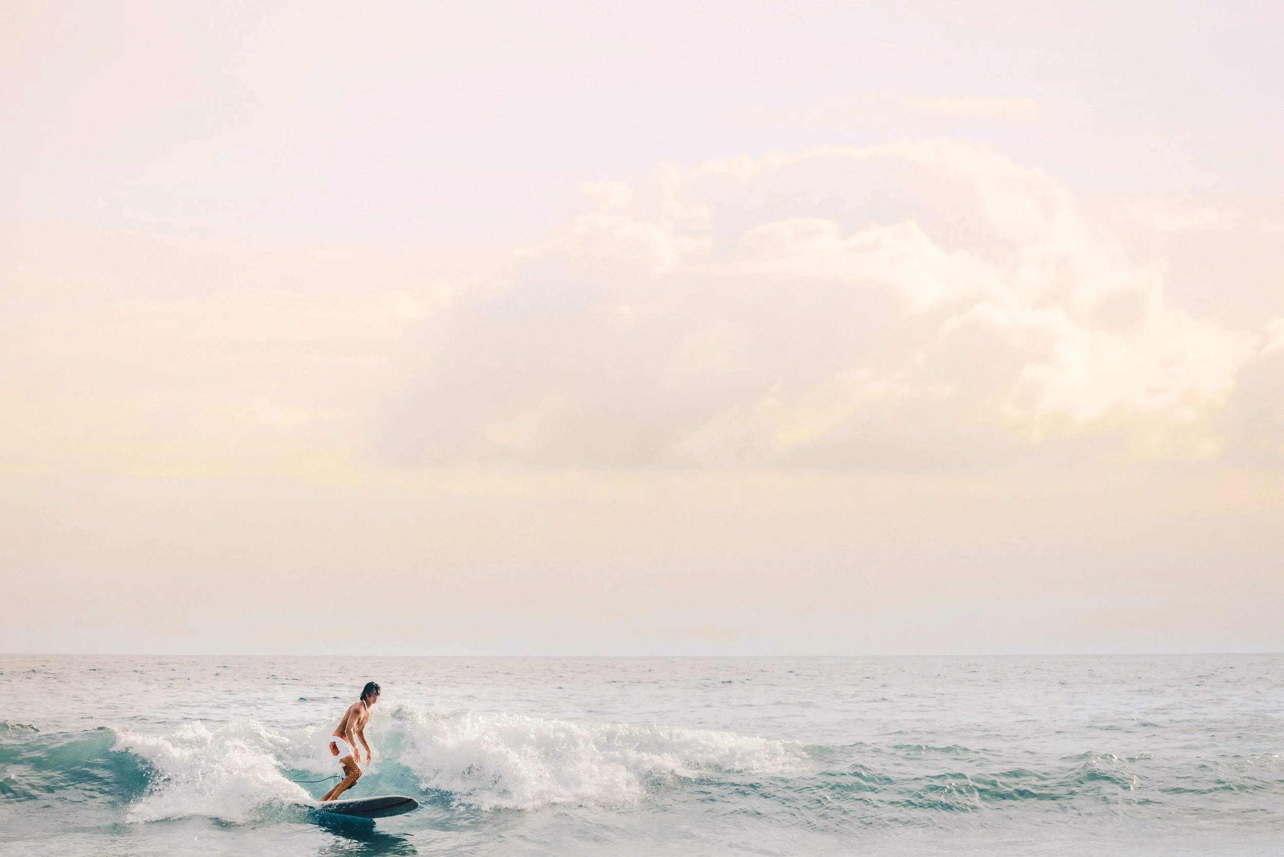 A person surfing on the ocean with the sky and clouds in the background.