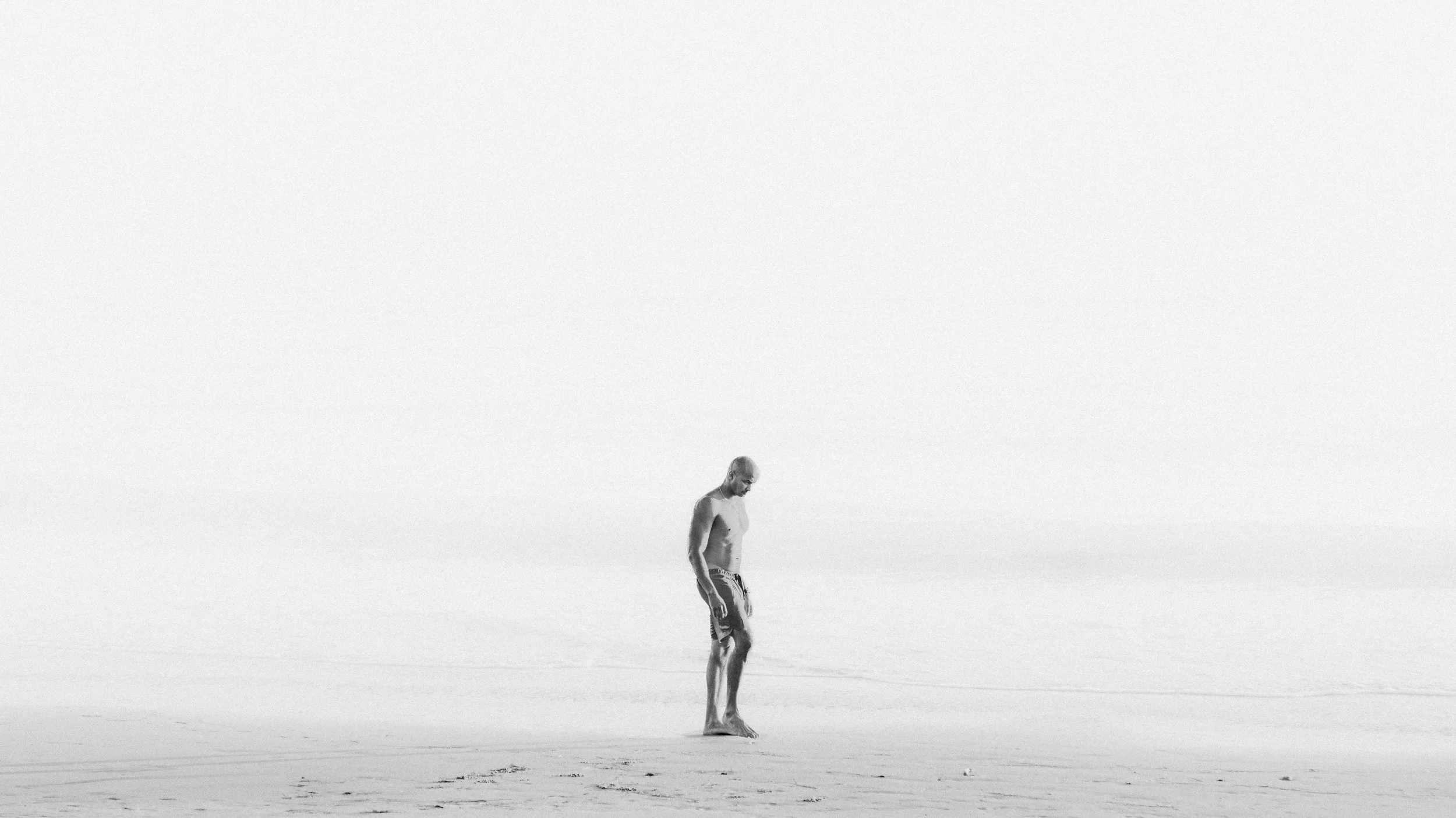 A man standing alone on a vast, empty landscape with a blank, featureless sky.