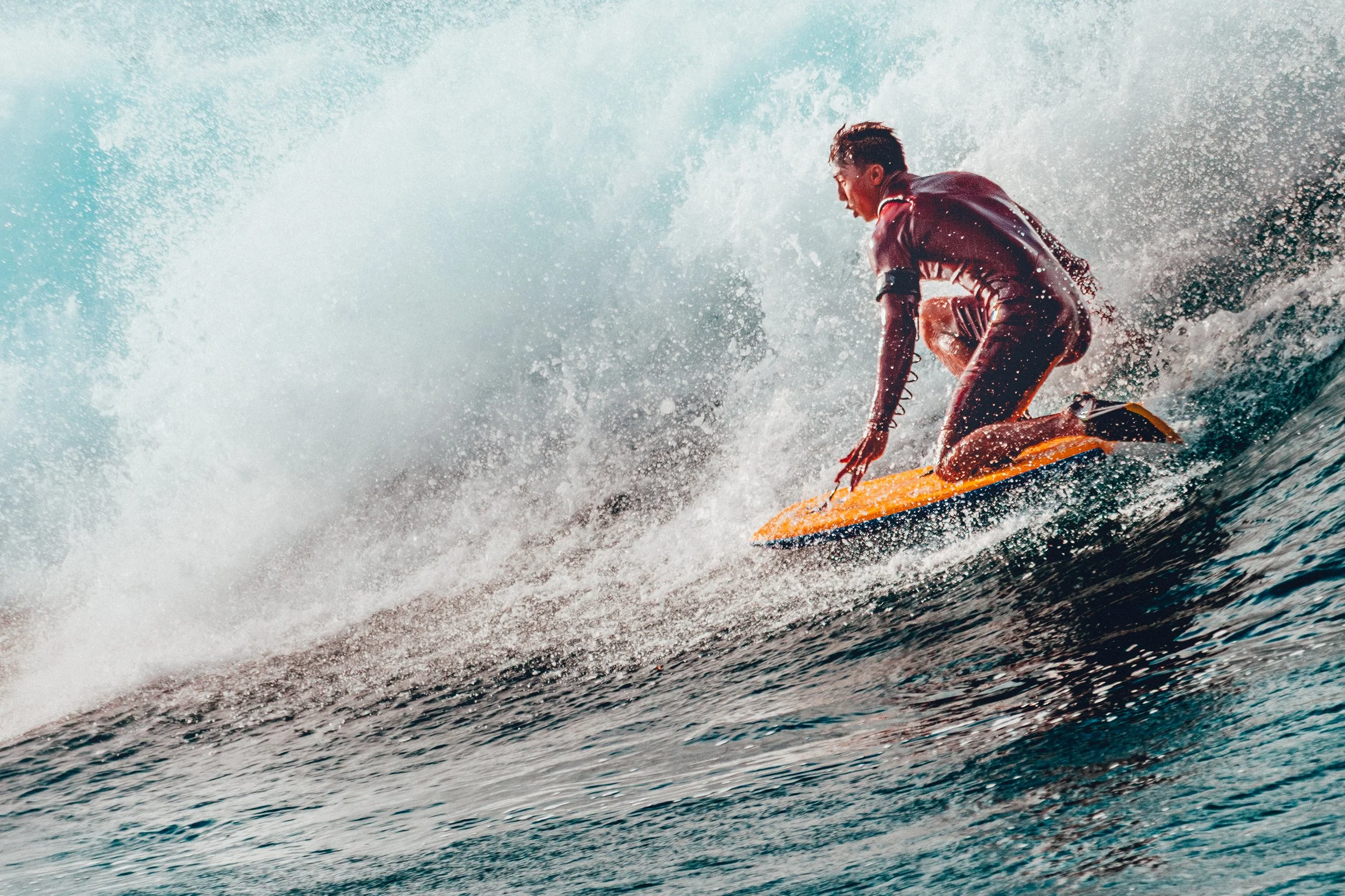 A person surfing on a wave in the ocean, crouching on a yellow surfboard wearing a wetsuit.