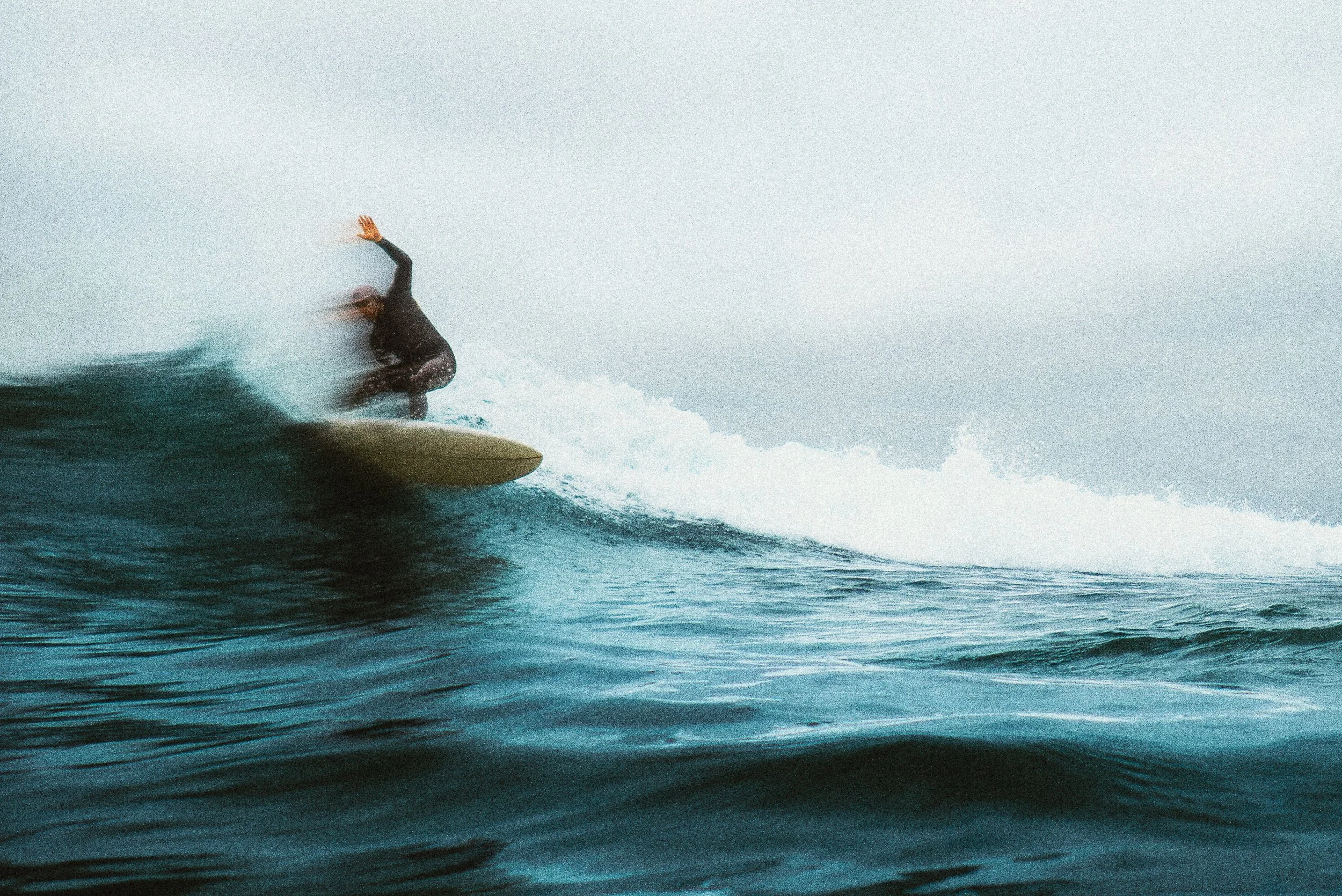 A surfer in black wetsuit riding a wave with water spray and white foam.