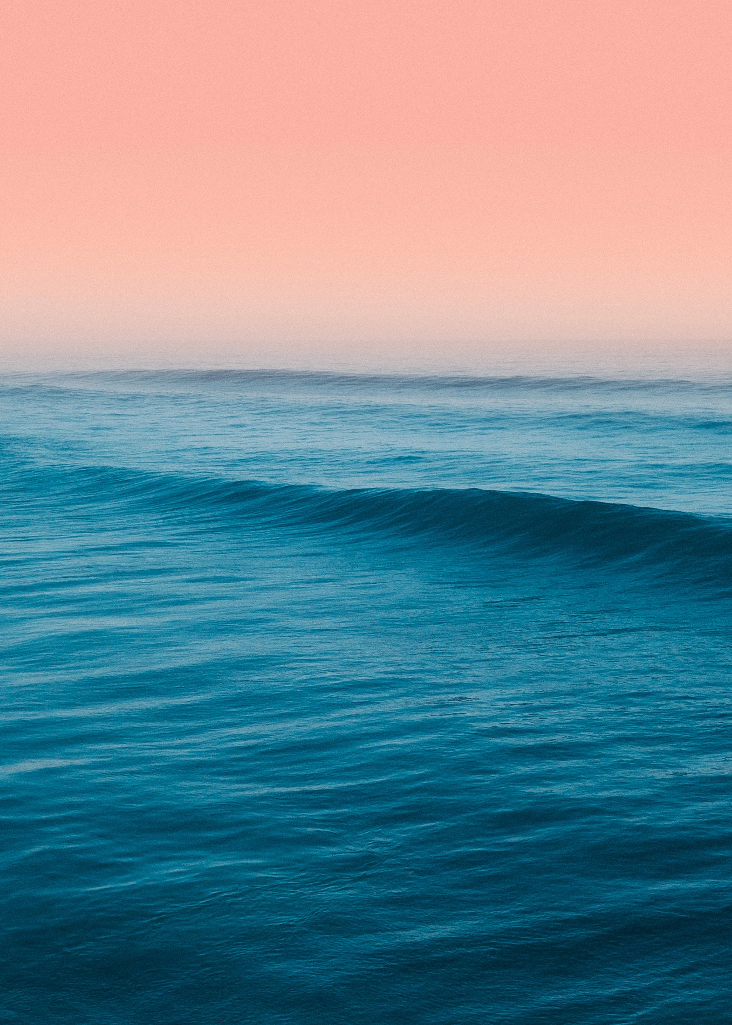 A calm ocean with gentle waves under a pinkish sky, possibly at sunrise or sunset.