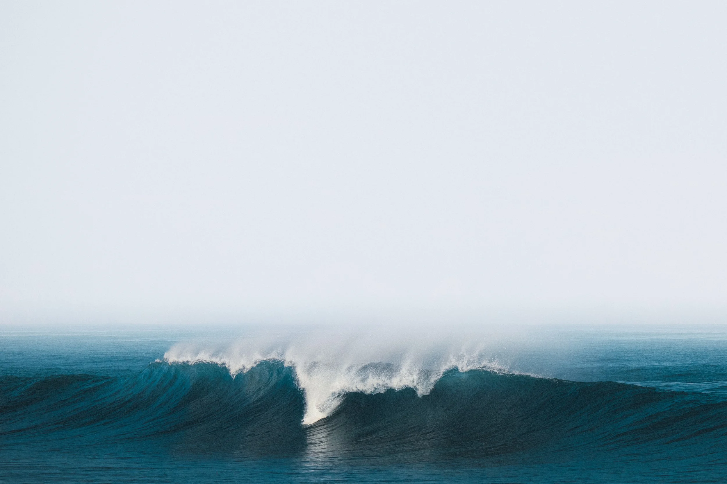 Large ocean waves crashing in the sea with a cloudy sky overhead.