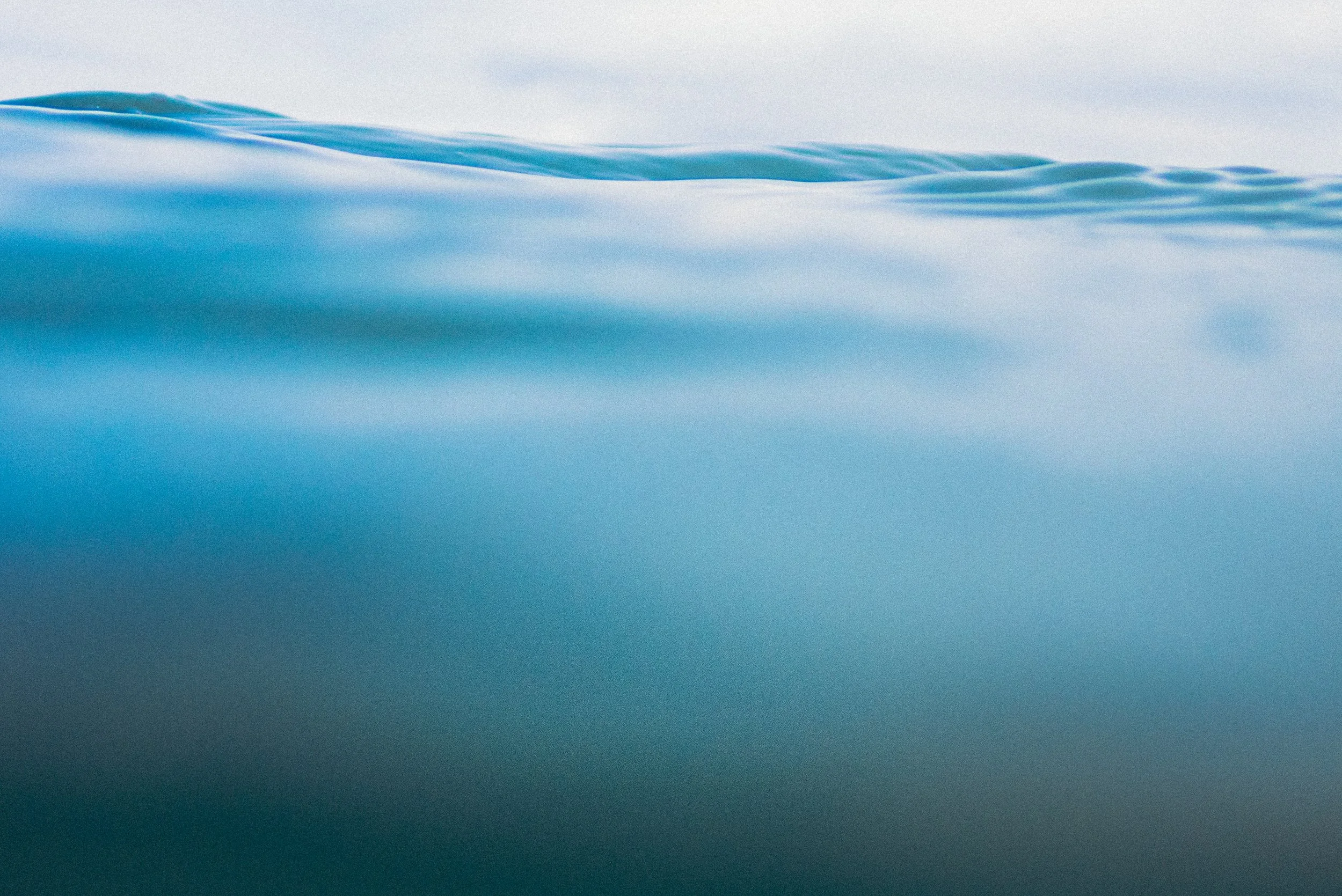 Close-up of cold, soft blue ice or snow with smooth, slightly rippled surface and a light gray sky in the background.