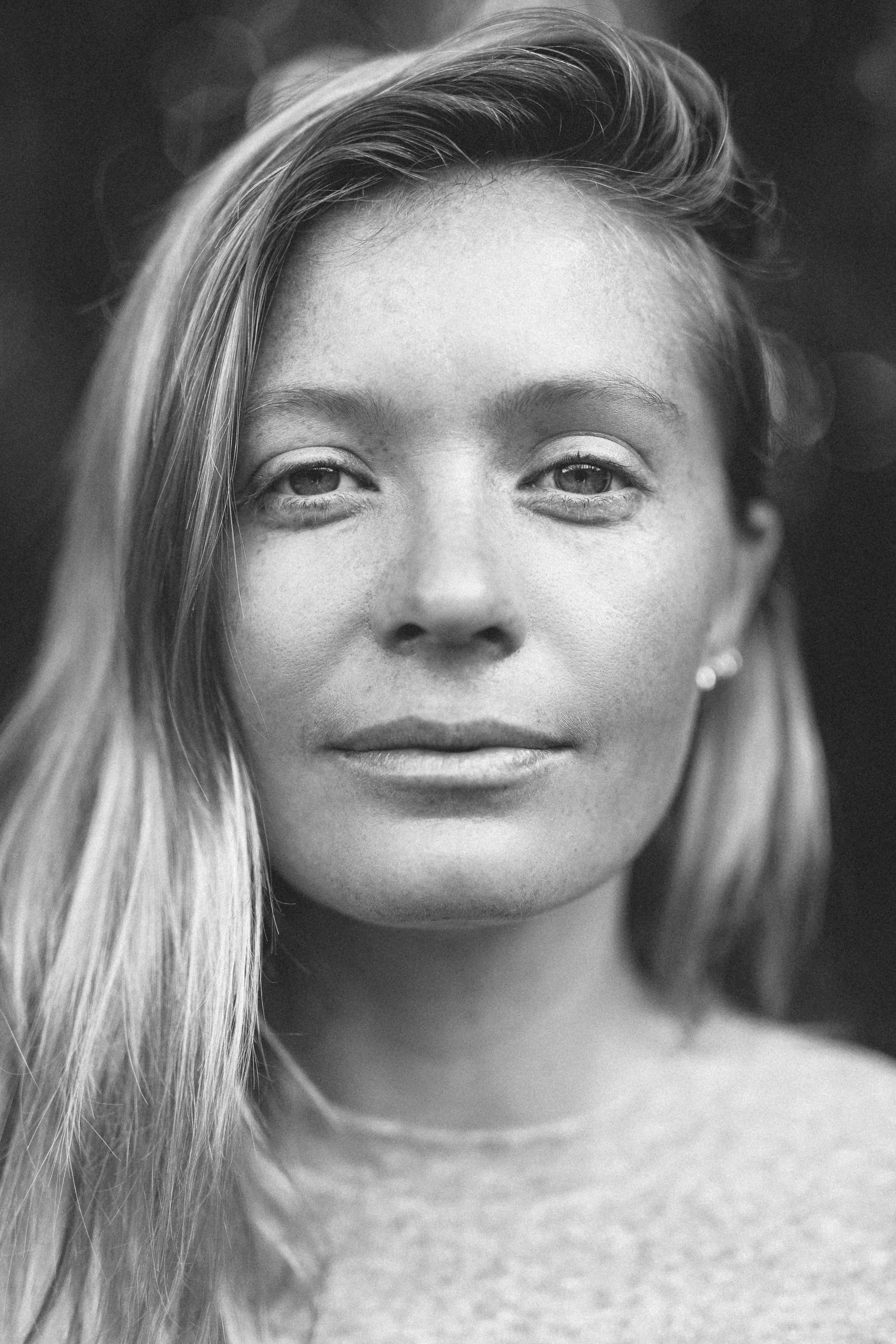 Close-up black and white portrait of a woman with long, straight hair, faint makeup, and a calm expression.