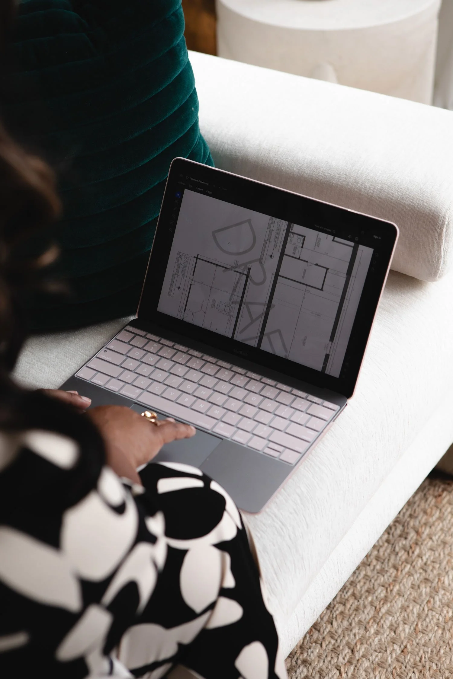 Person using a tablet with architectural plans, sitting on a white upholstered surface with a green cushion nearby.