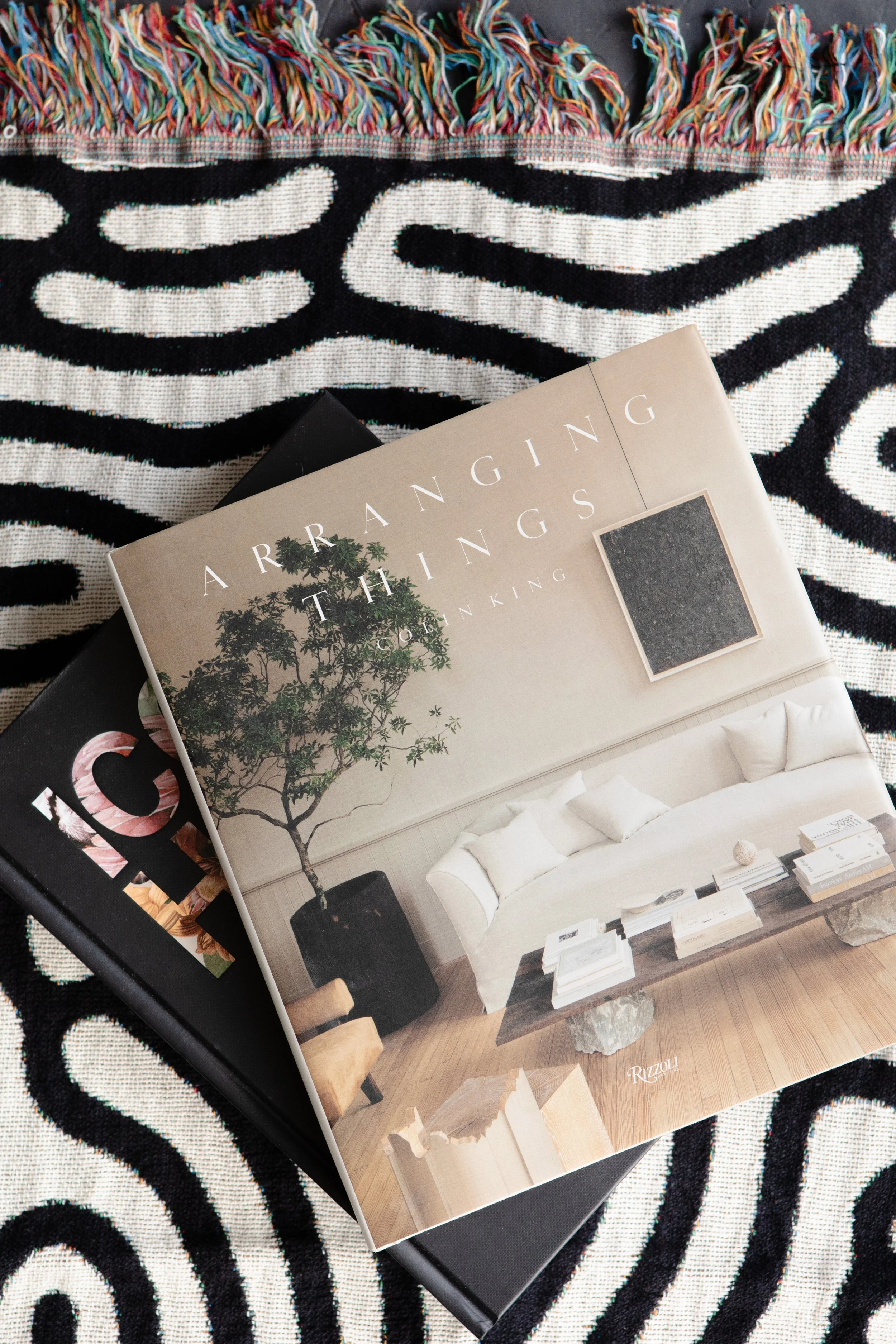 A catalog displaying modern living room furniture with a white sofa, a black side table, a beige rug, and wooden accents, placed on a black and white patterned rug.
