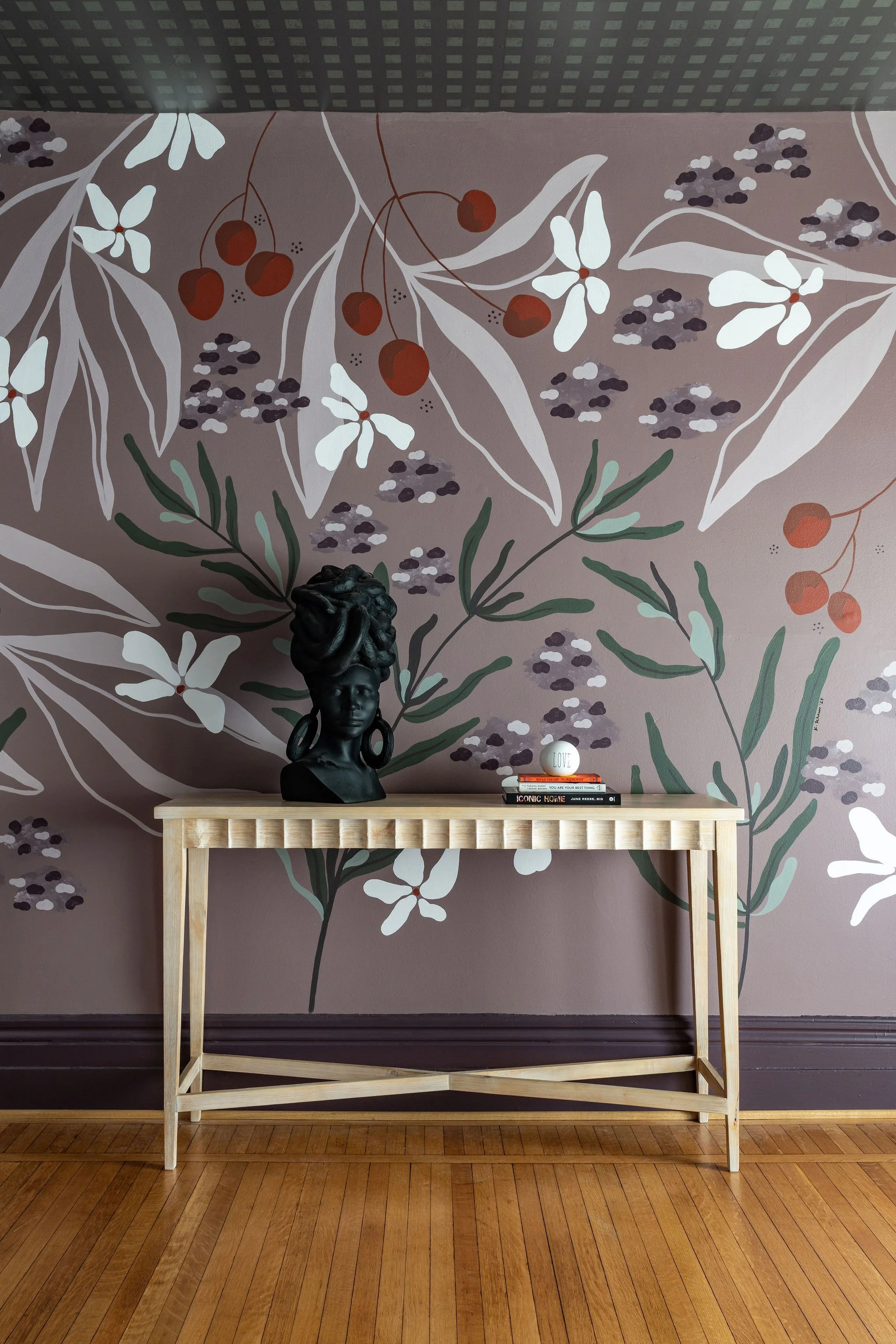 Interior decor with a wooden table against a floral wallpapered wall. The table has a black bust of a woman with dreadlocks, a stack of books, and a decorative ball with the word 'LOVE' on it.