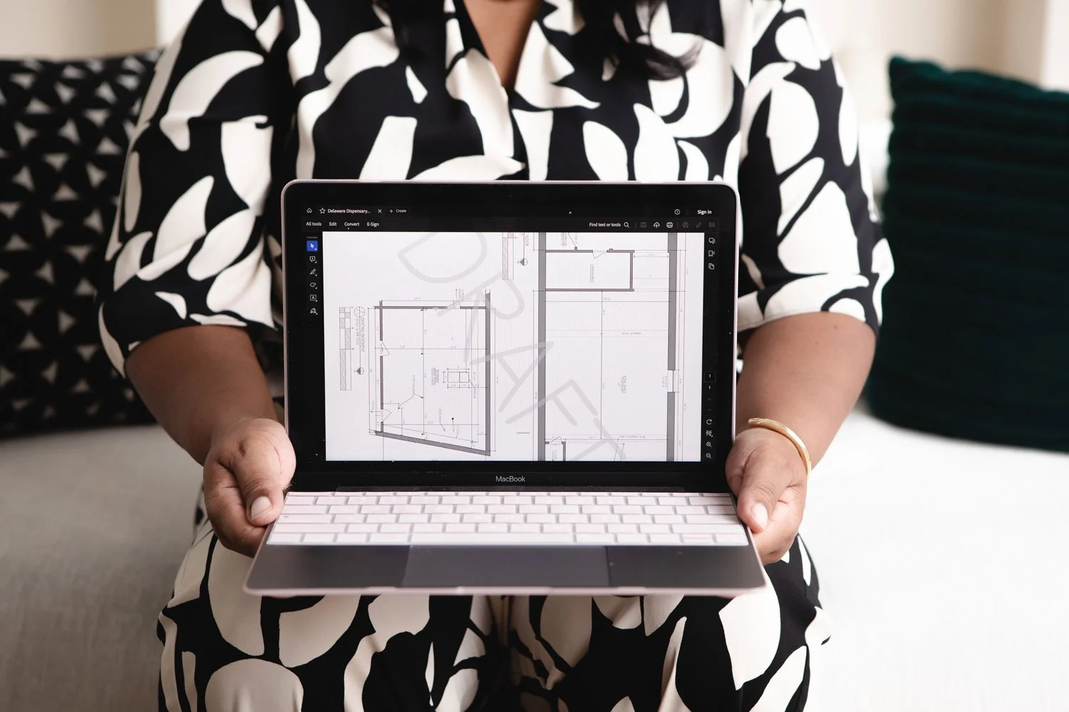 Person holding a MacBook displaying architectural blueprints or floor plans.
