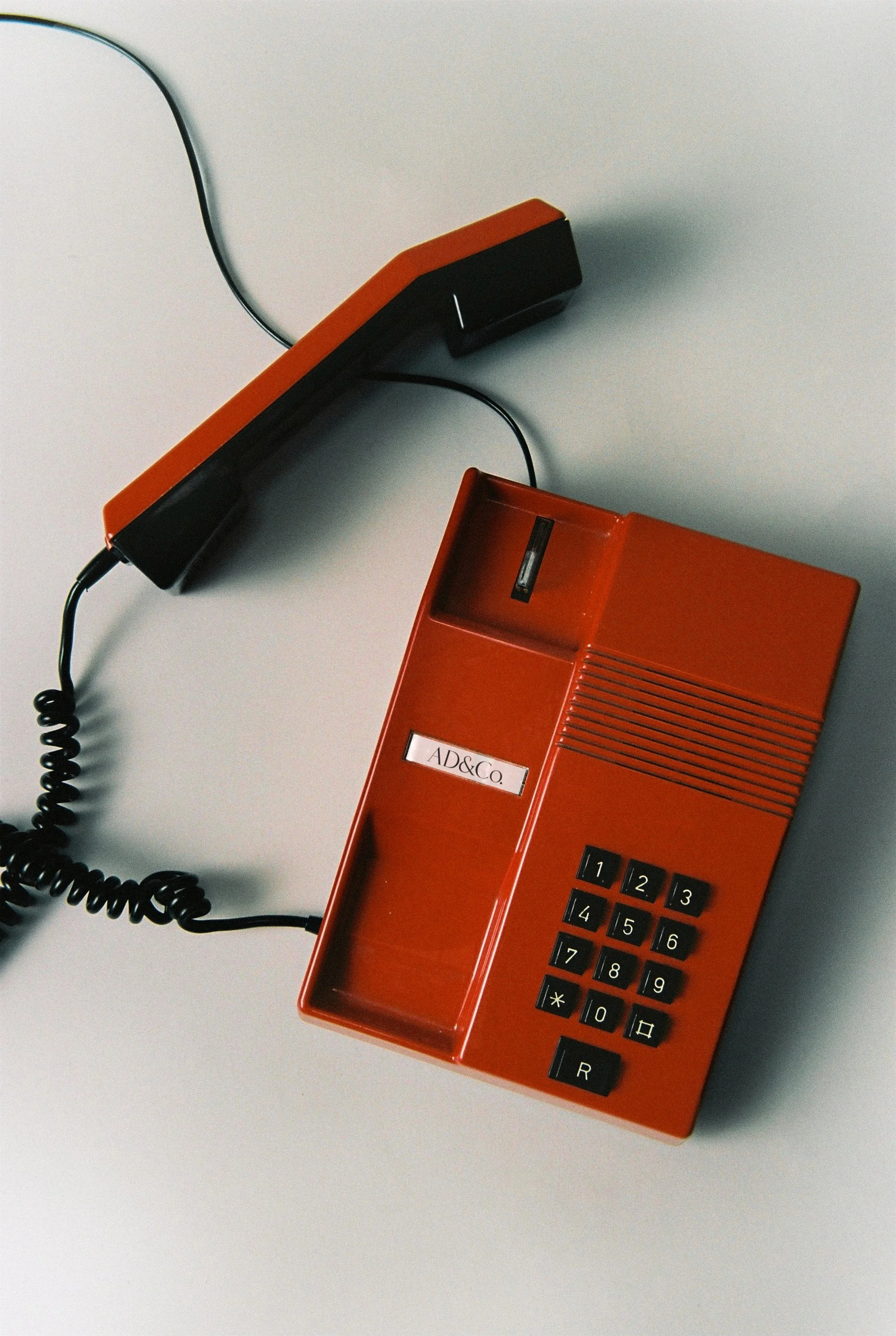 A vintage red rotary telephone with a black keypad, placed on a white surface.