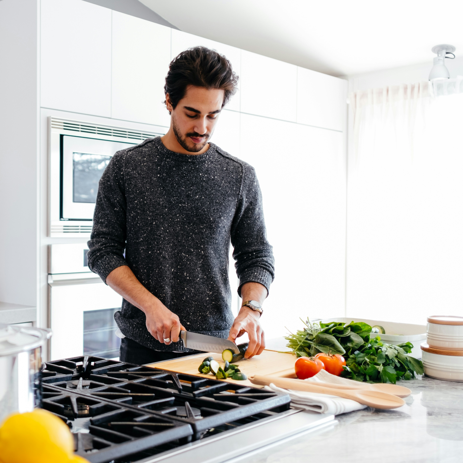 A man chopping zucchini on a cutting board in a modern kitchen with fresh vegetables on the counter. He represents an Immunity IV Drip patient which prevents illness and boosts the immune system.