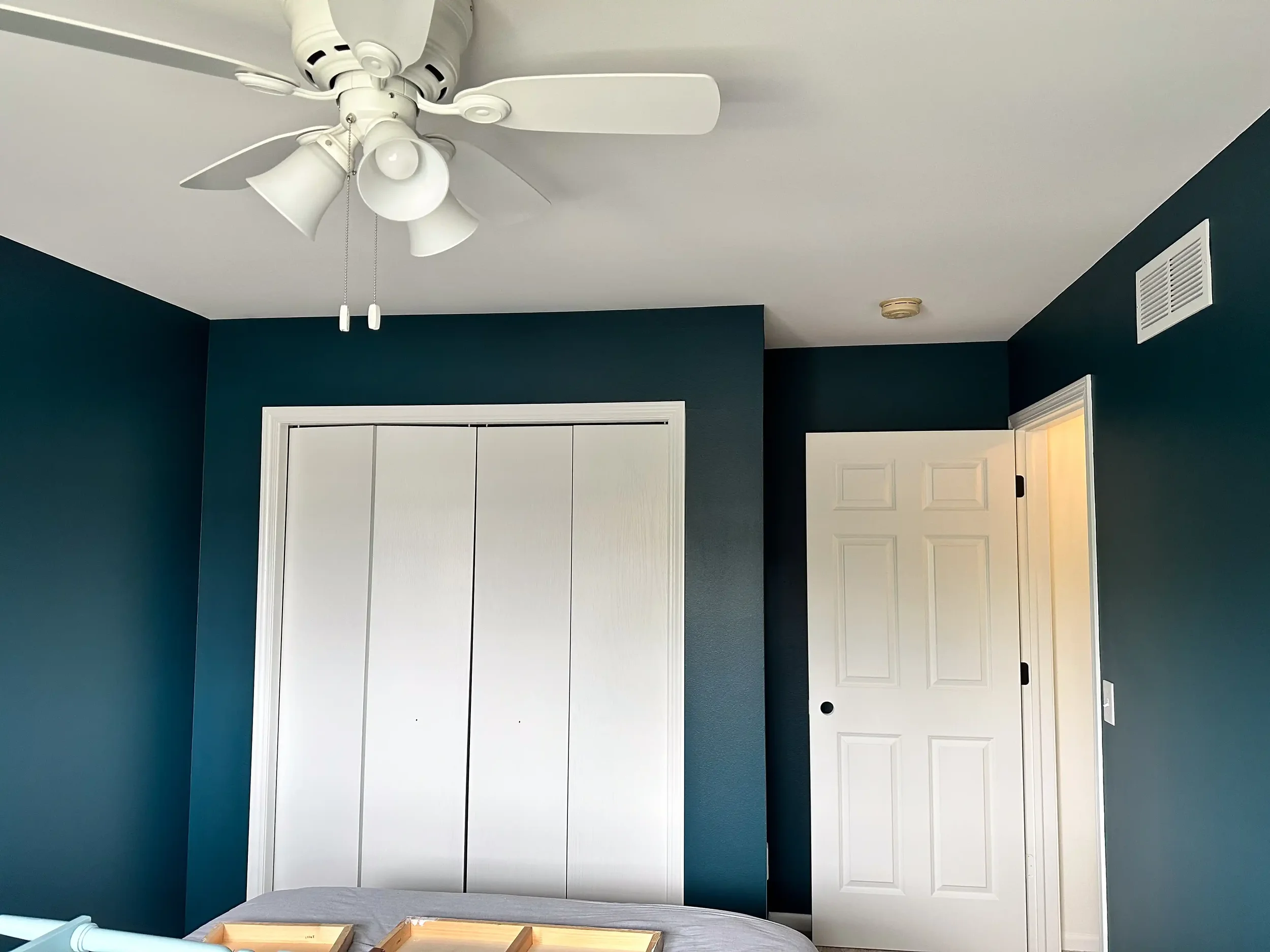 A ceiling fan with light fixtures and chains in a room with dark teal walls, white doors, and vents.