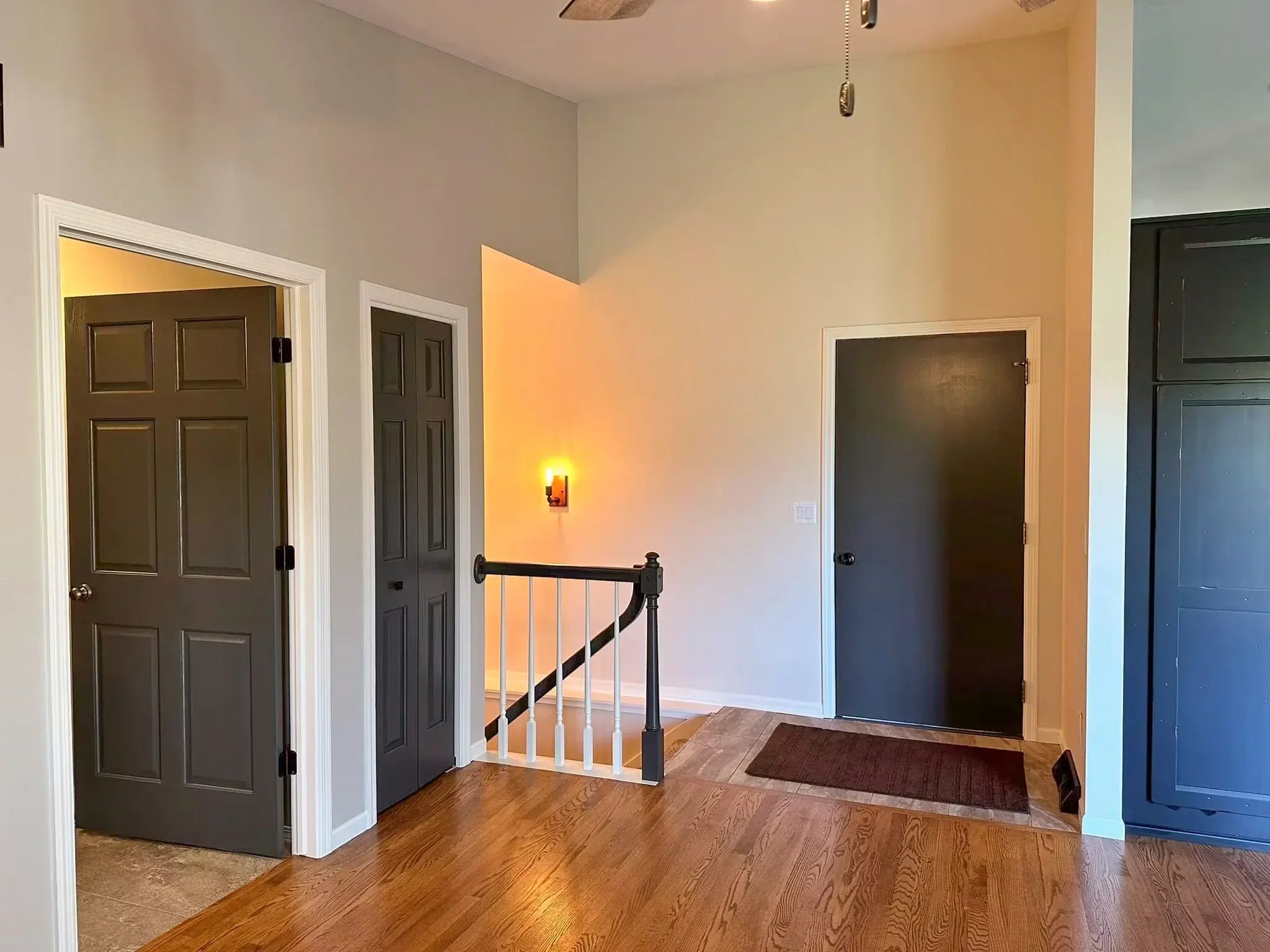 Entryway with wooden floors, white walls, black doors, a staircase with white pickets, and a brown rug.