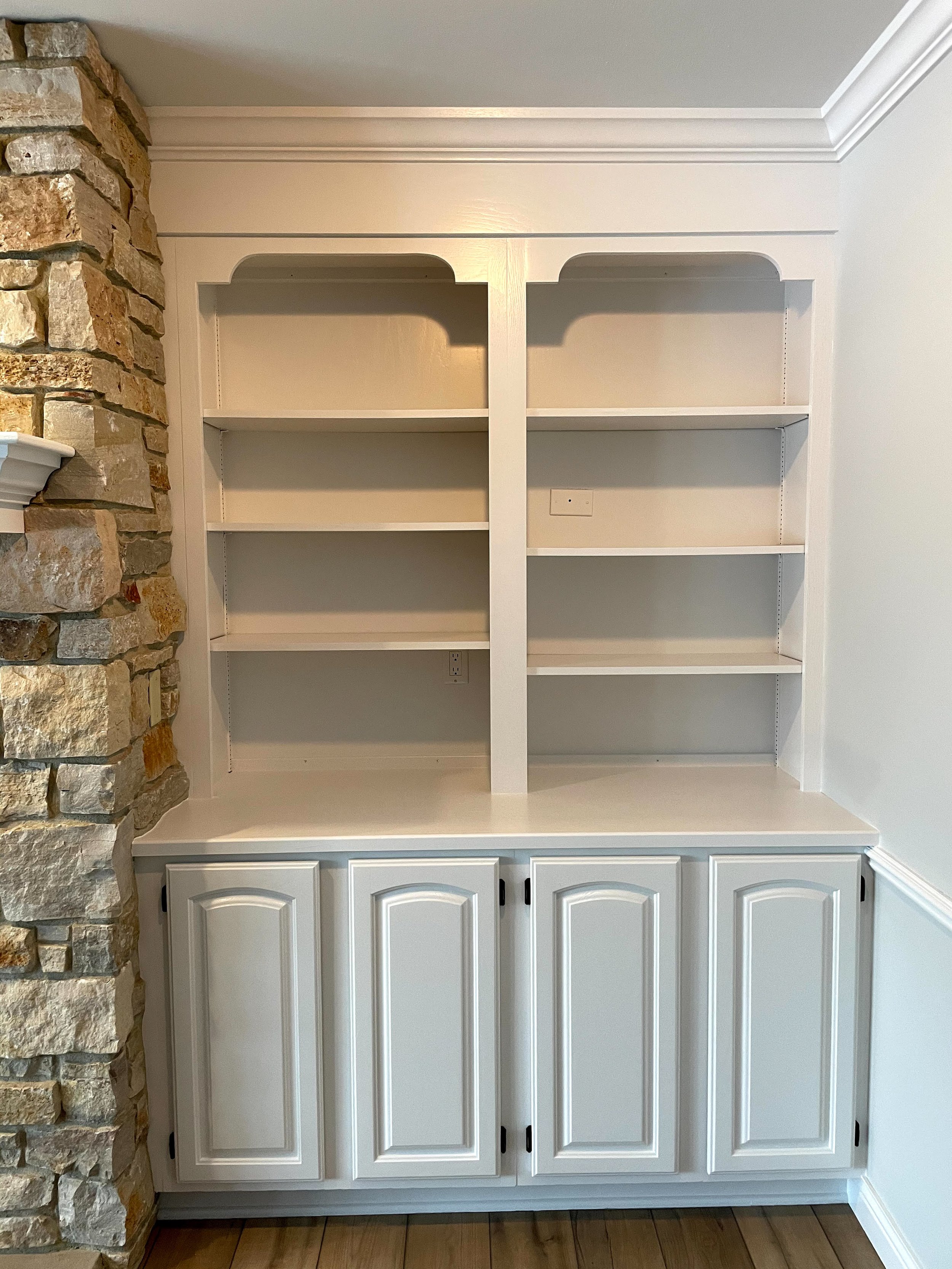 White built-in bookshelf with three shelves and cabinet doors below, situated next to a stone wall.