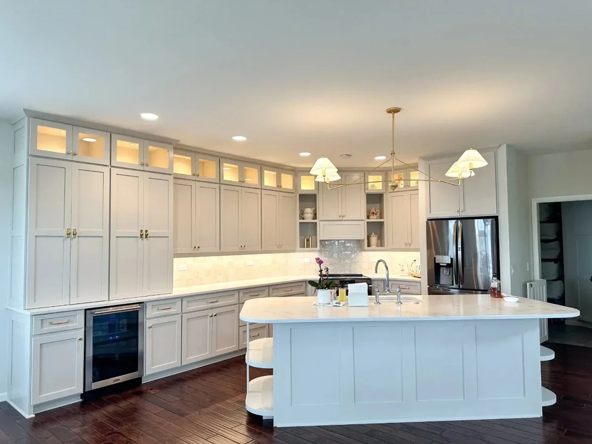 Modern kitchen with white cabinetry, marble island, wine cooler, stainless steel refrigerator, dark hardwood floors, and chandelier lighting.