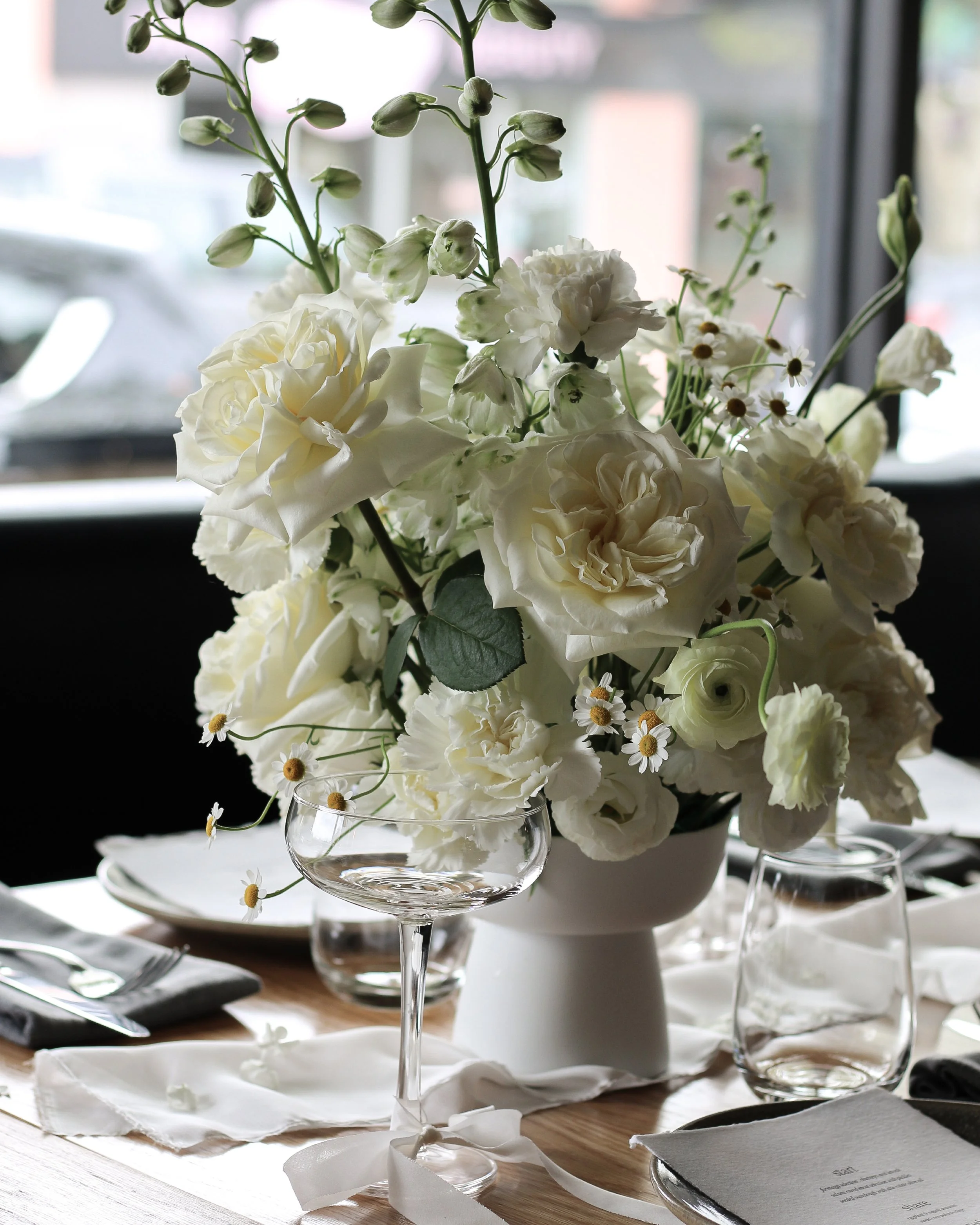 Elegant white floral centerpiece on a dining table with glassware and table setting.
