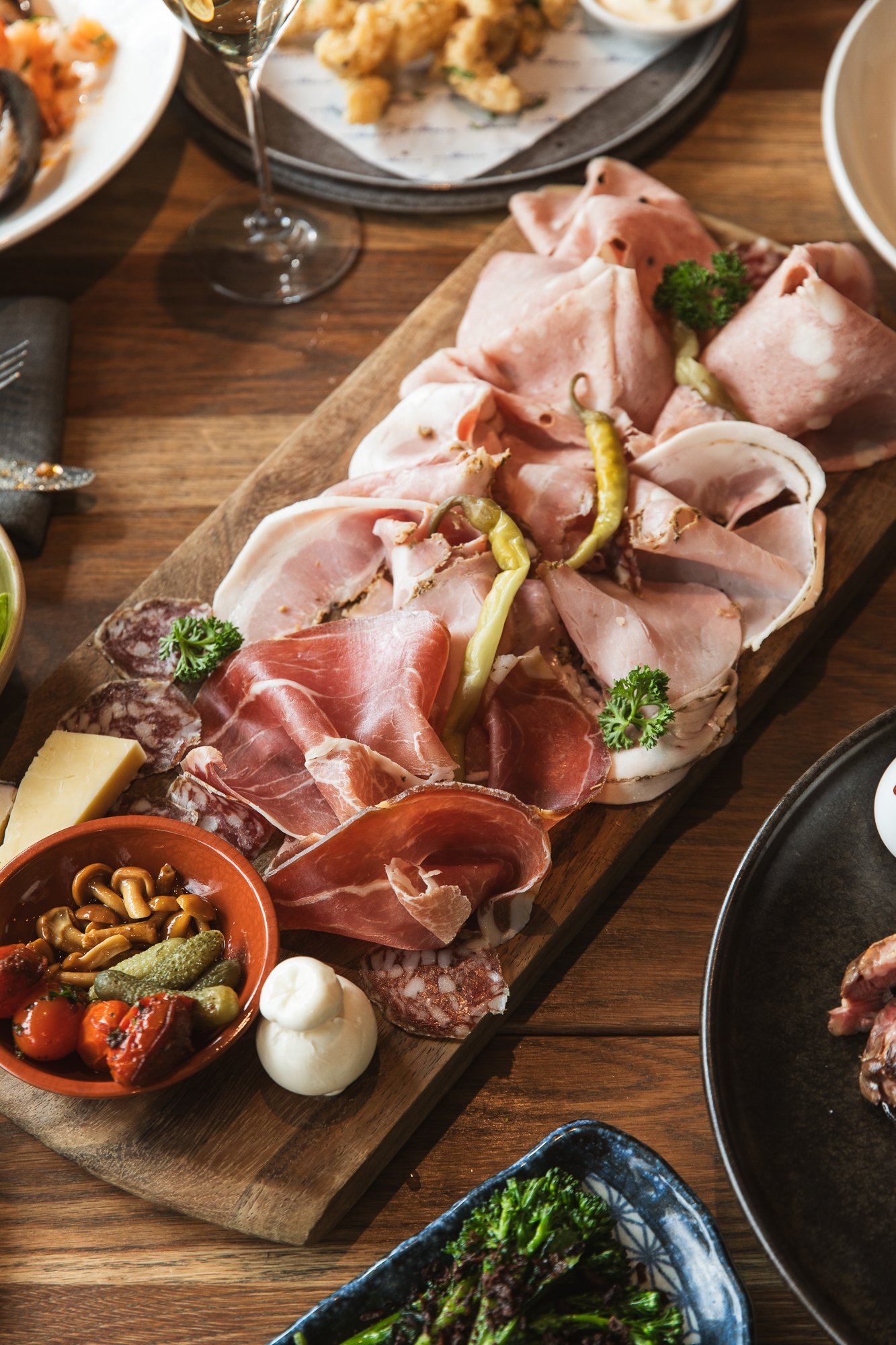 Assorted cured meats, pickles, cheese, and vegetables on a wooden serving board at a local Italian restaurant located in Mornington.