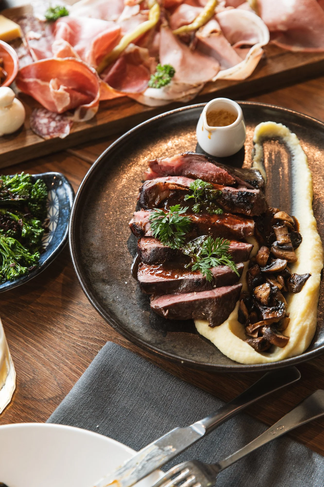 A generous steak, mushrooms, and mashed potatoes, garnished with herbs on a black plate in Main Street, Mornington.