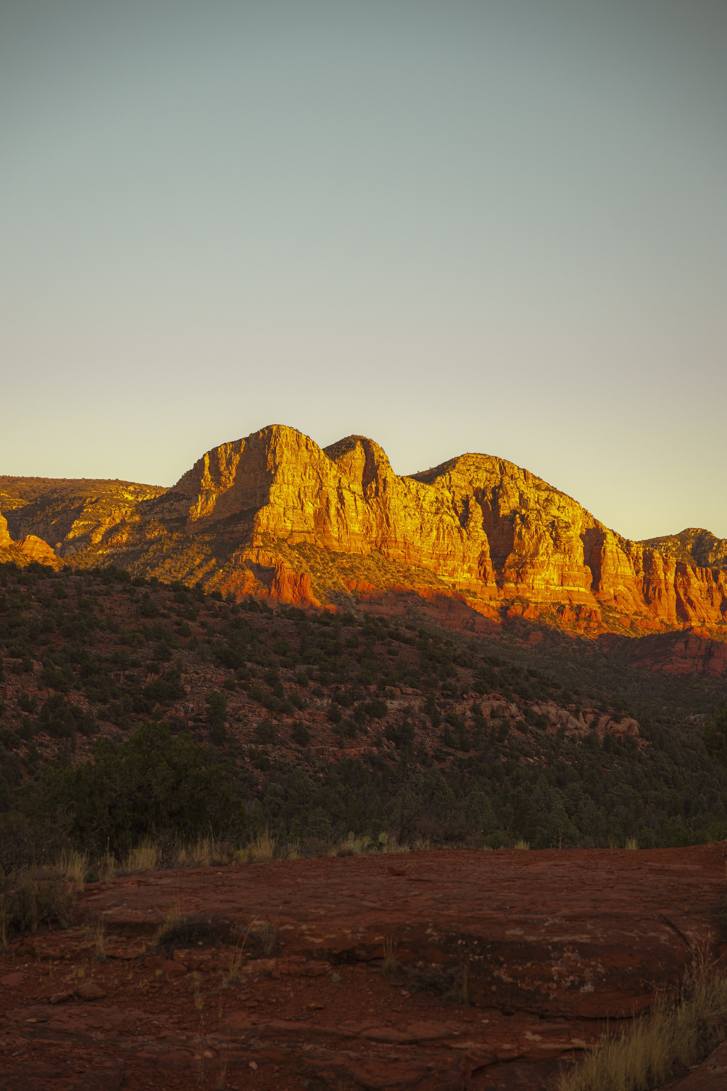 Sunlit red rock mountains with sparse vegetation at sunset