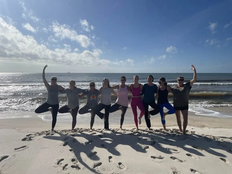 Yogis on the beach supporting one another in tree pose at Dauphin Island Alabama
