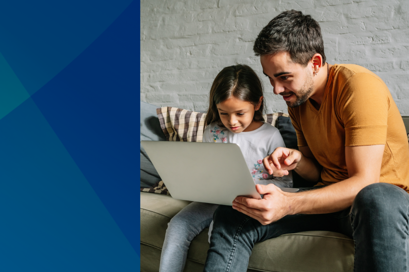 A dad and his daughter on a sofa with a laptop.