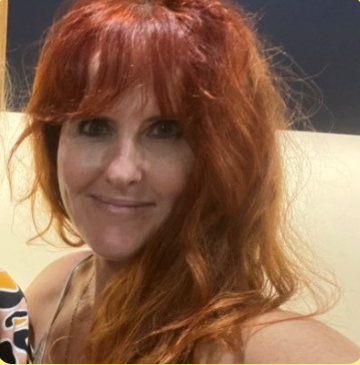 A woman with long, wavy red hair smiling at the camera.
