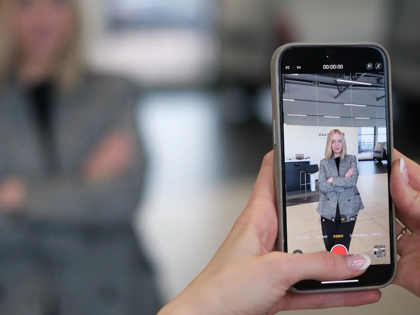 Person filming a woman with a smartphone inside an office or waiting area.