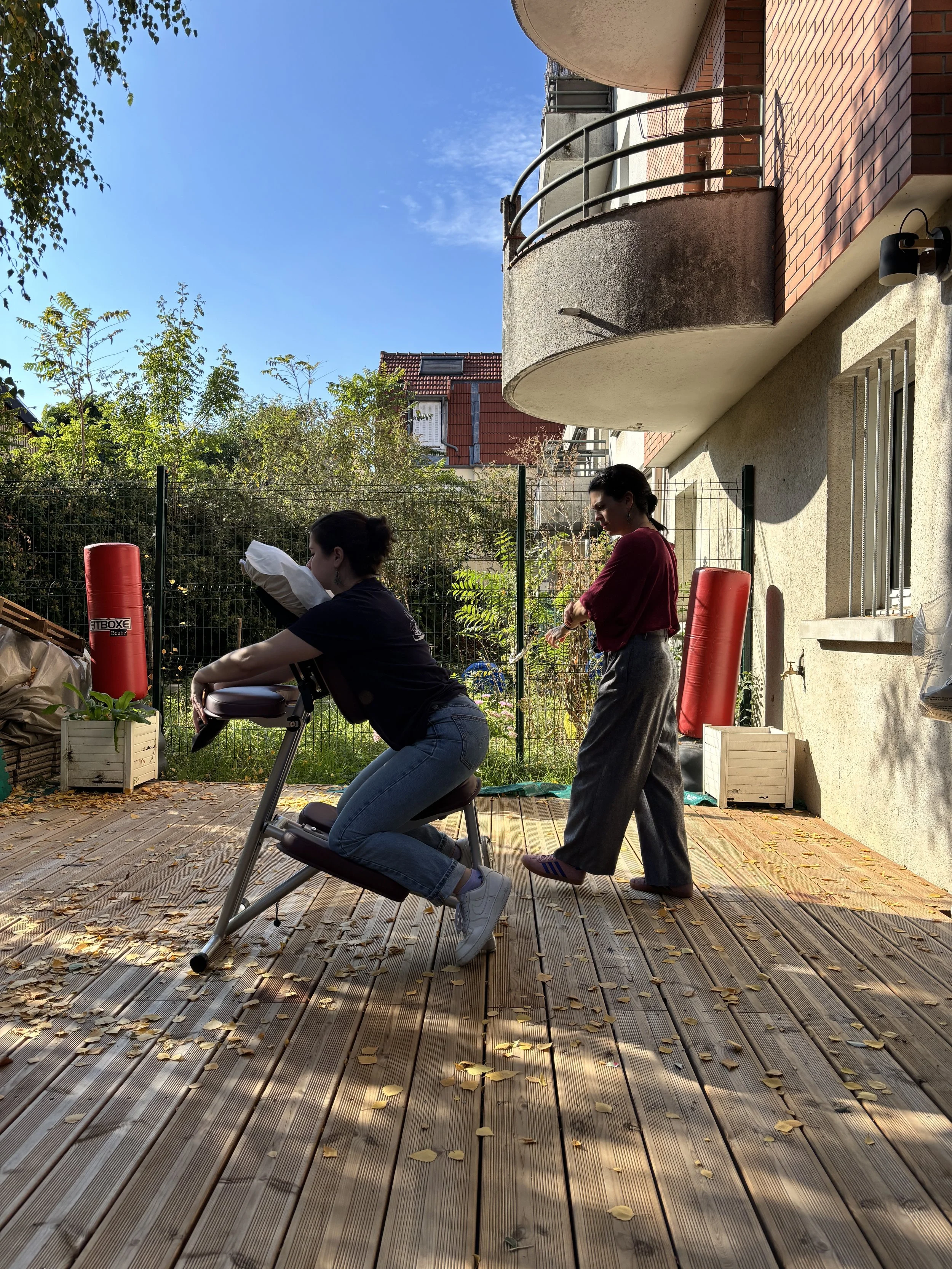 Deux femmes s'entraînent sur une terrasse en bois avec des équipements de boxe, sous un ciel bleu avec quelques nuages.