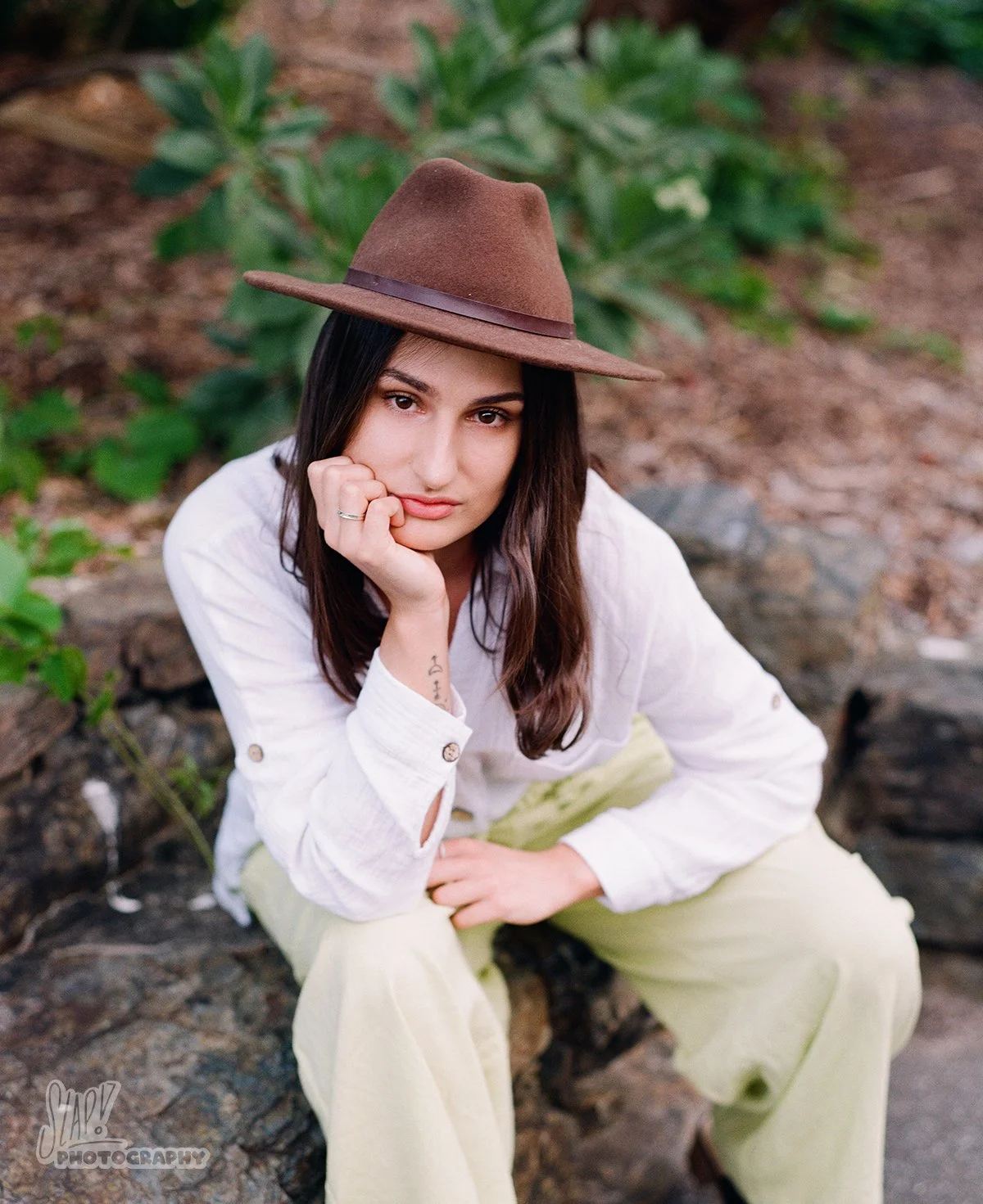Pretty young woman sitting in loose fitting shirt and slacks with brown felt hat