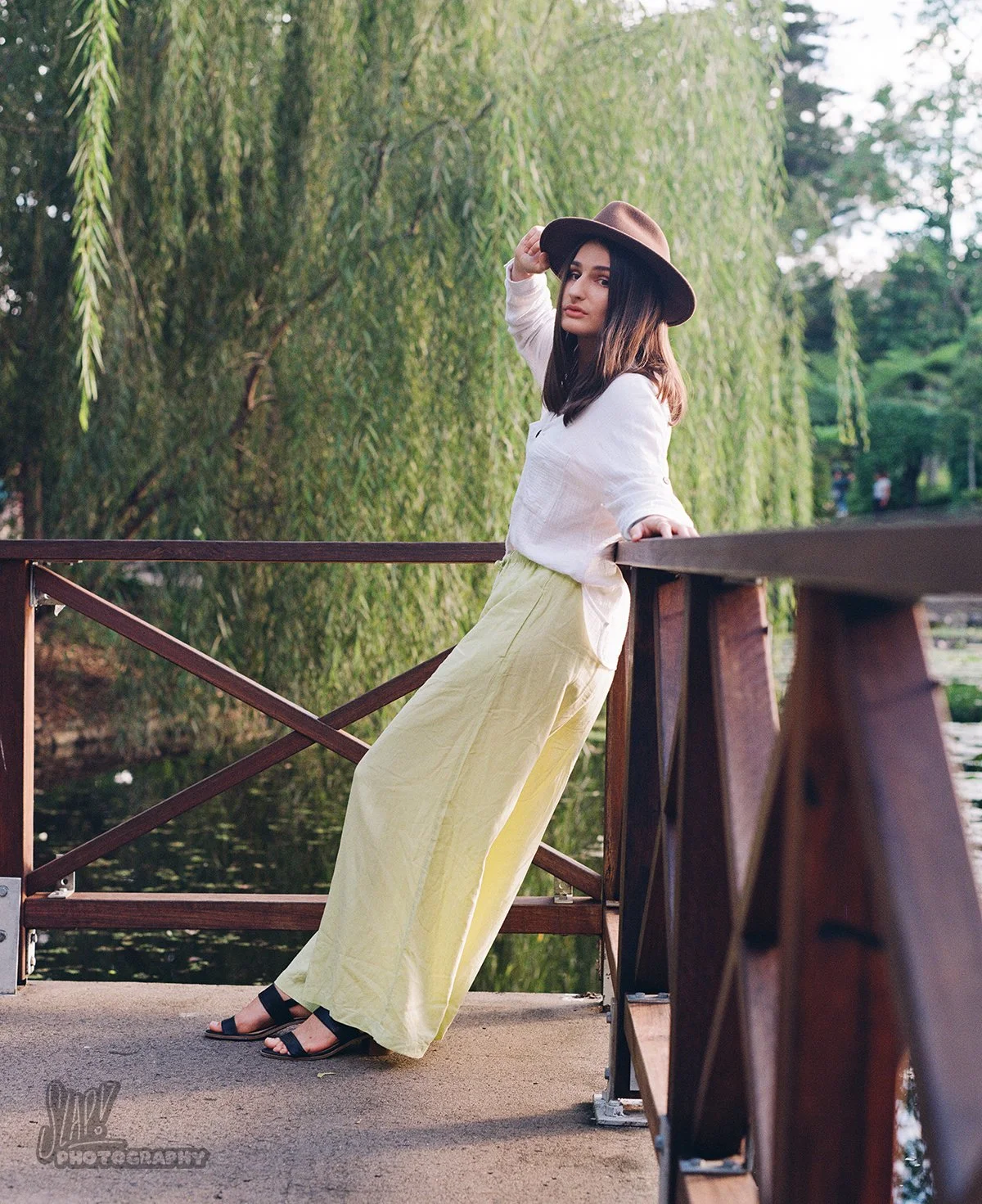 Pretty young lady in loose fitting outfit posing in front of willow tree