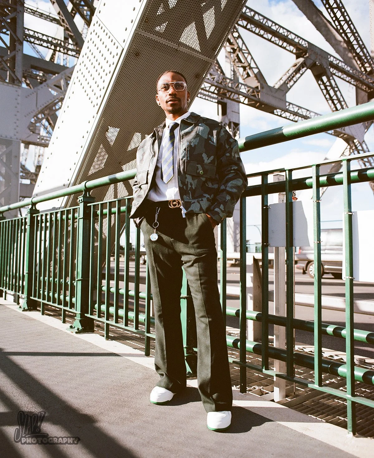 Nigerian influencer in camo jacket and wool trousers posing in front of rivetted structure