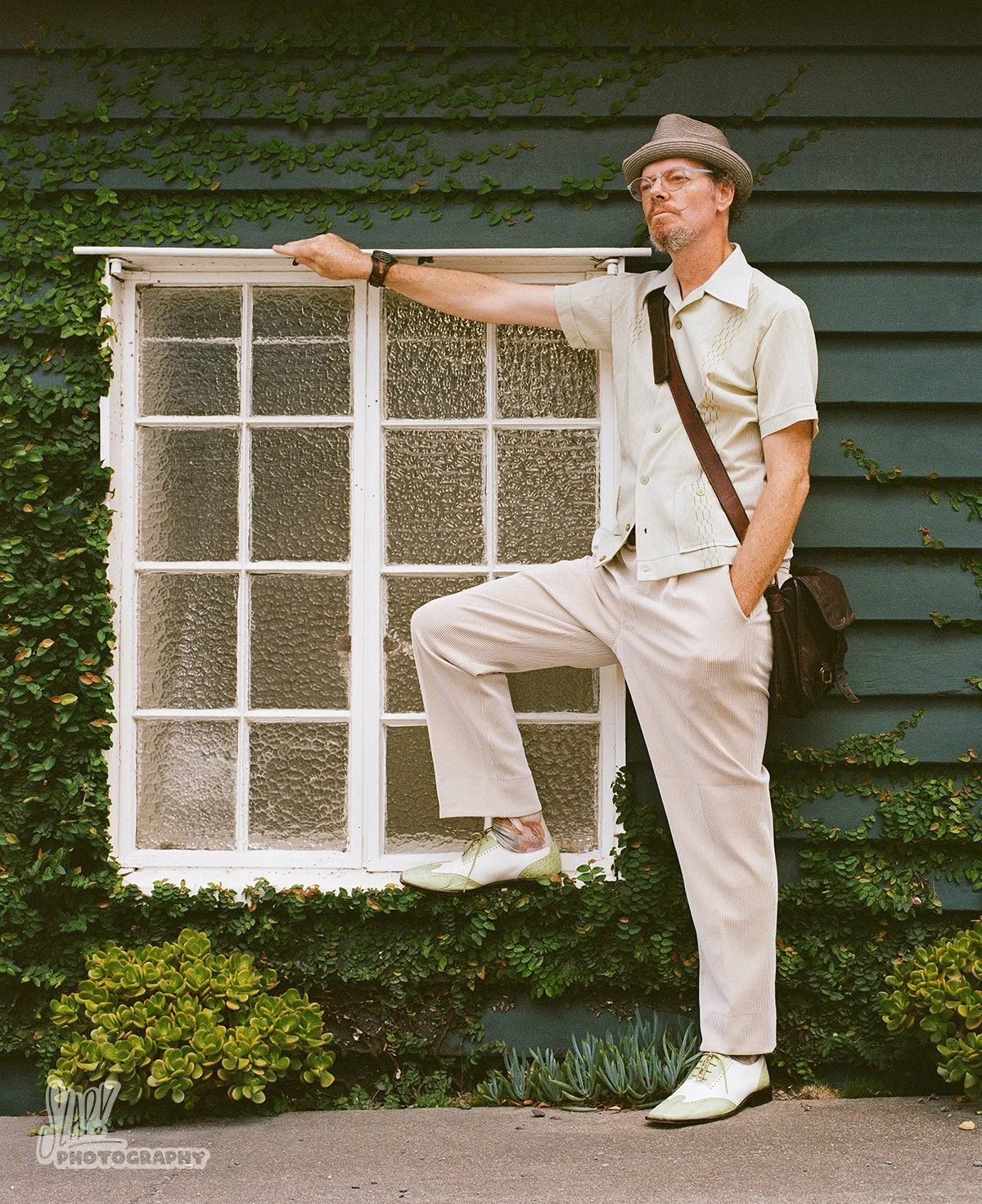 Dapper gentleman posing next to a window with a green wall
