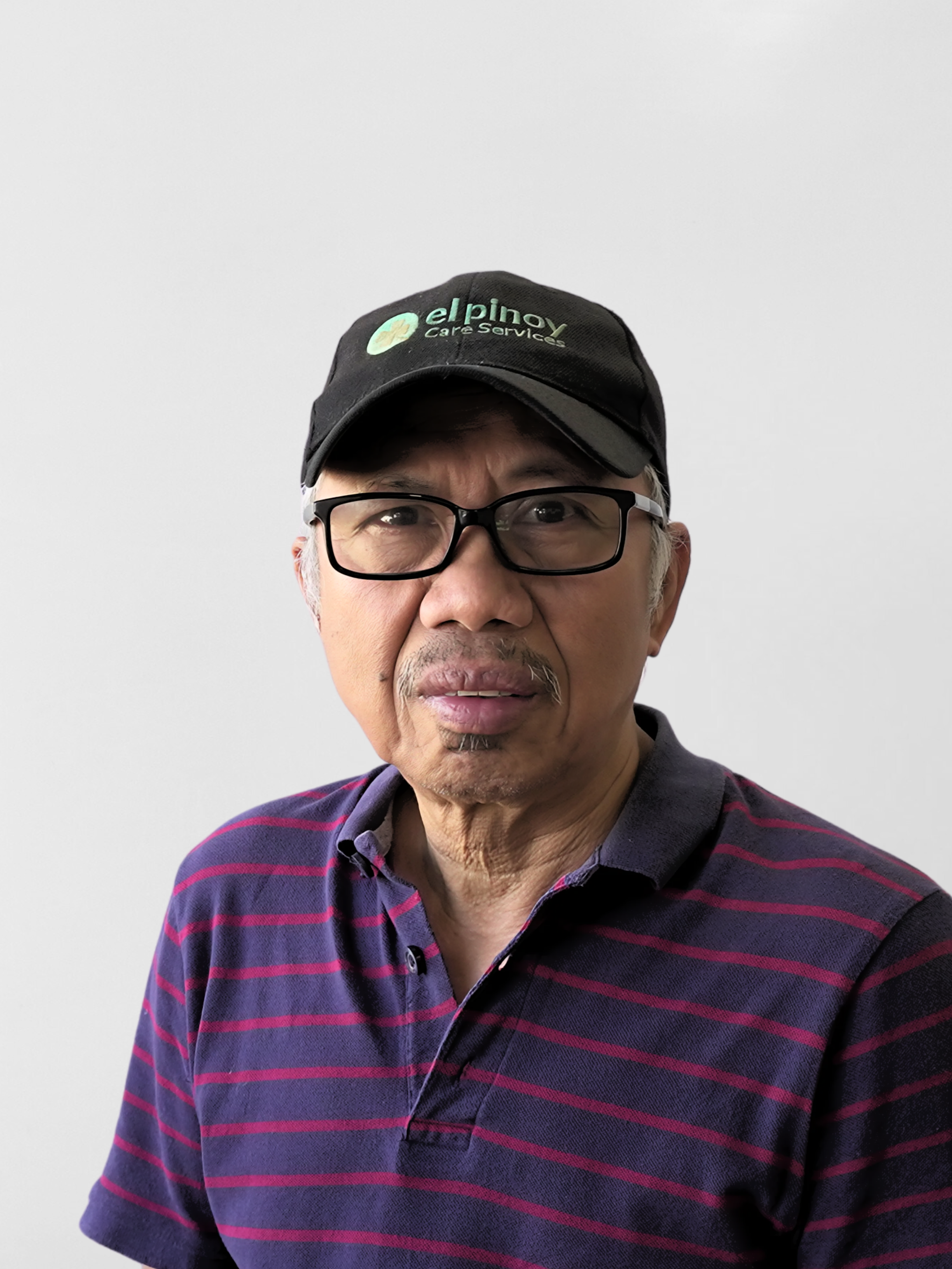 Man wearing glasses, a black cap, and a striped polo shirt against a plain background.