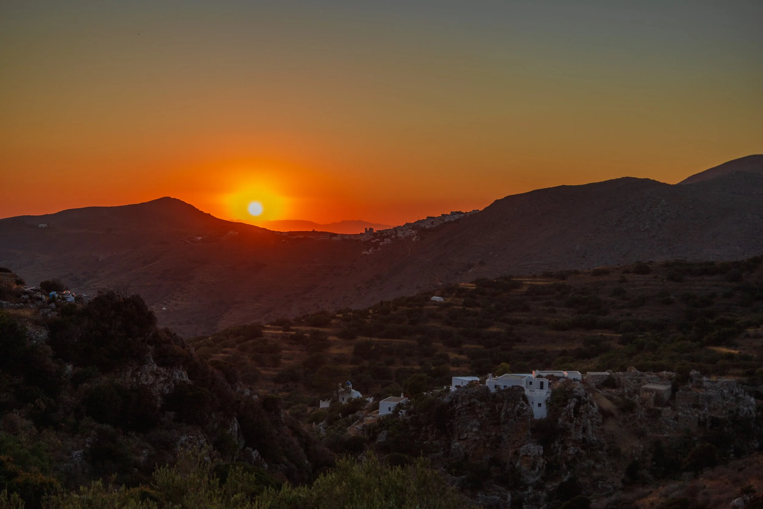 Sunset vista on northern Amorgos.
The buildings of Stroumbos lie in the foreground, ancient terraces behind them, and the village of Tholaria further back as the sun sets behind Naxos.
