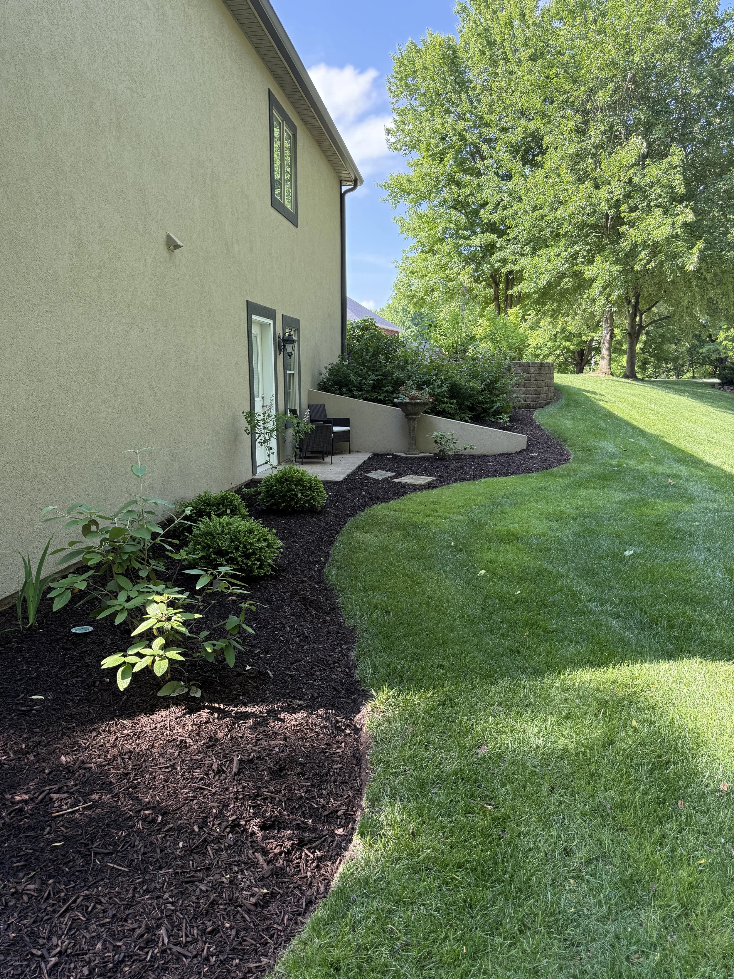 Curved mulch bed with shrubs and a clean lawn edge along the side of a home
