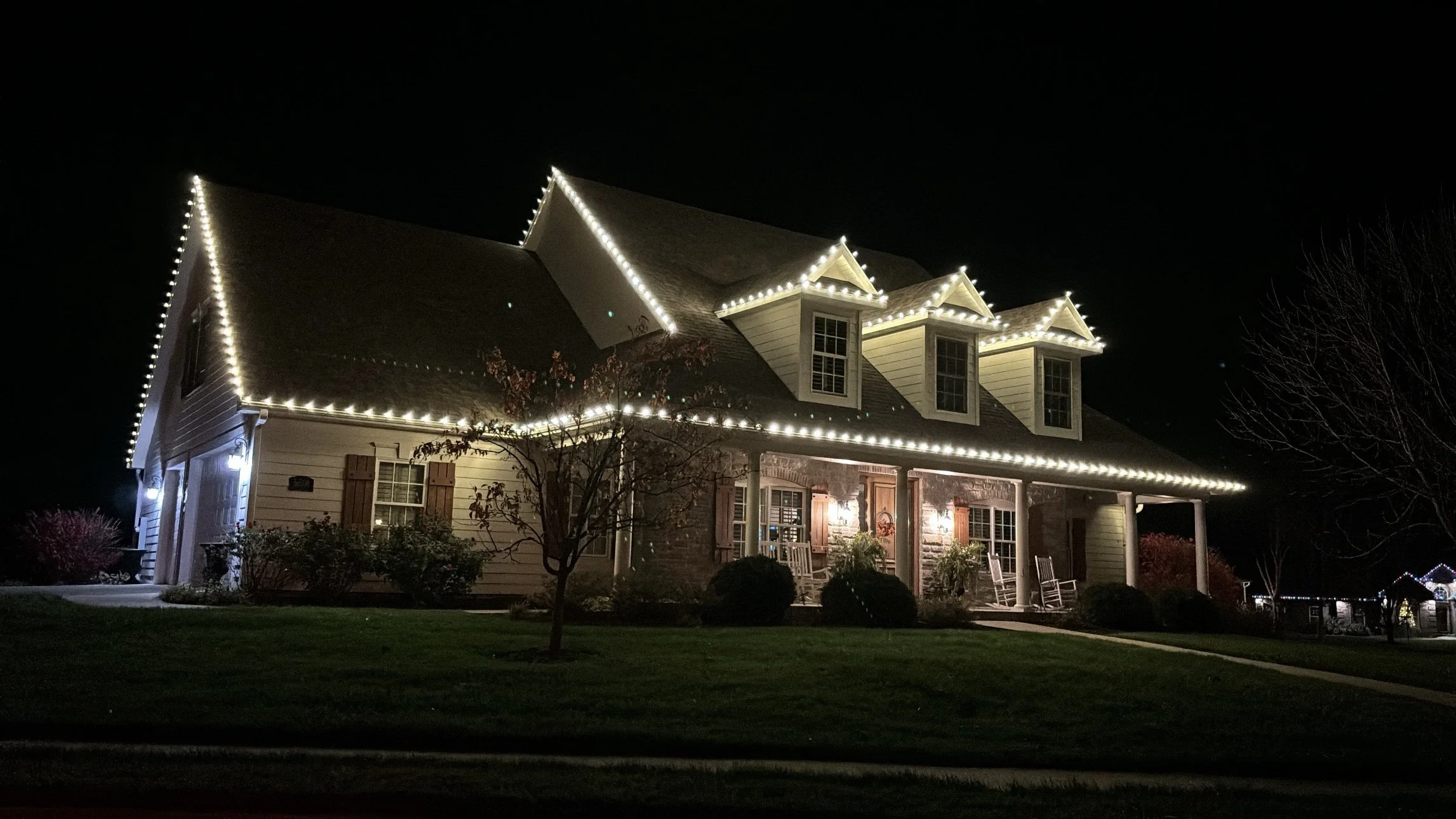 House at night with white Christmas lights outlining the roofline and dormers