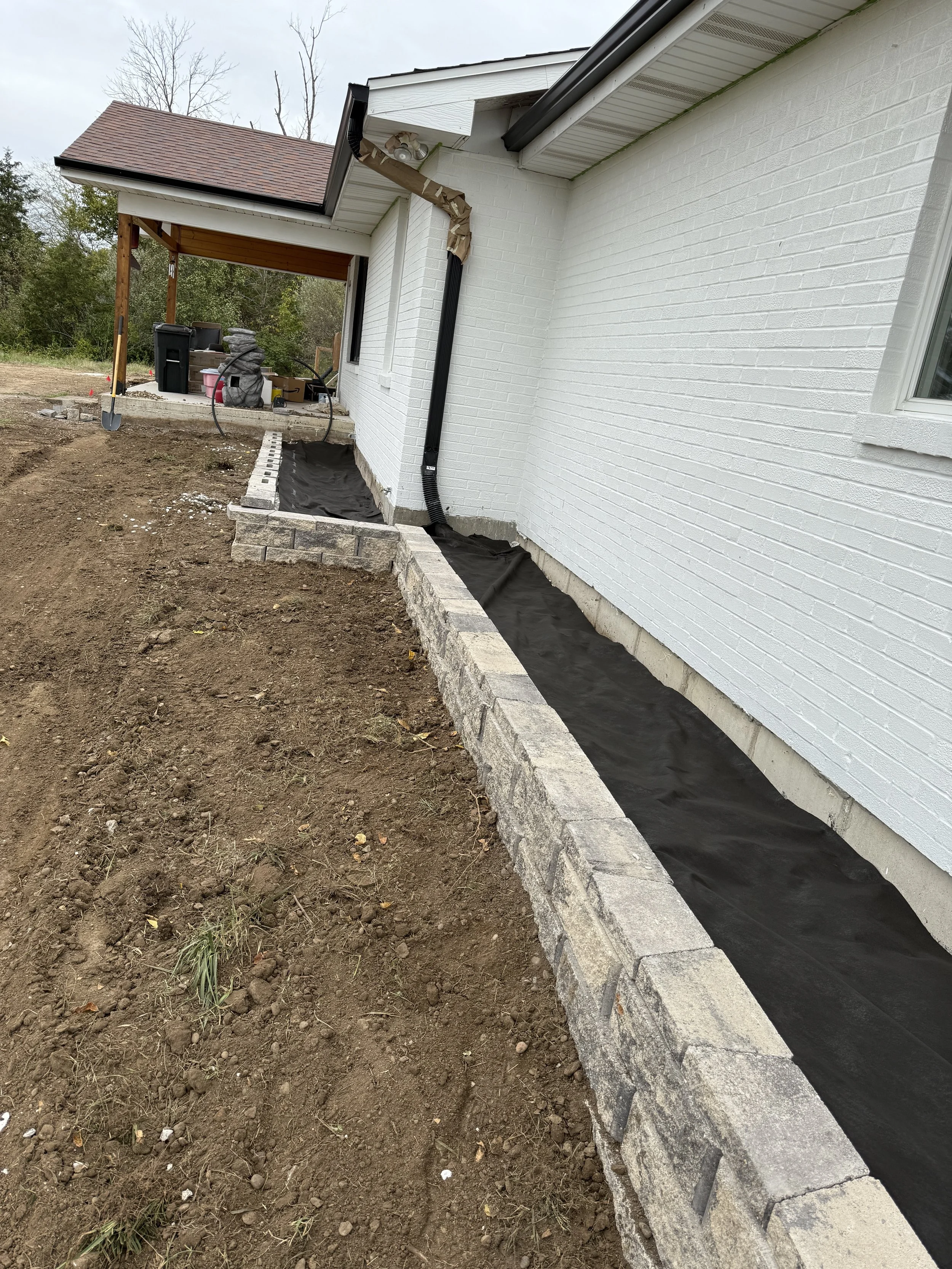 New stone retaining wall along the side of a white brick home during landscaping
