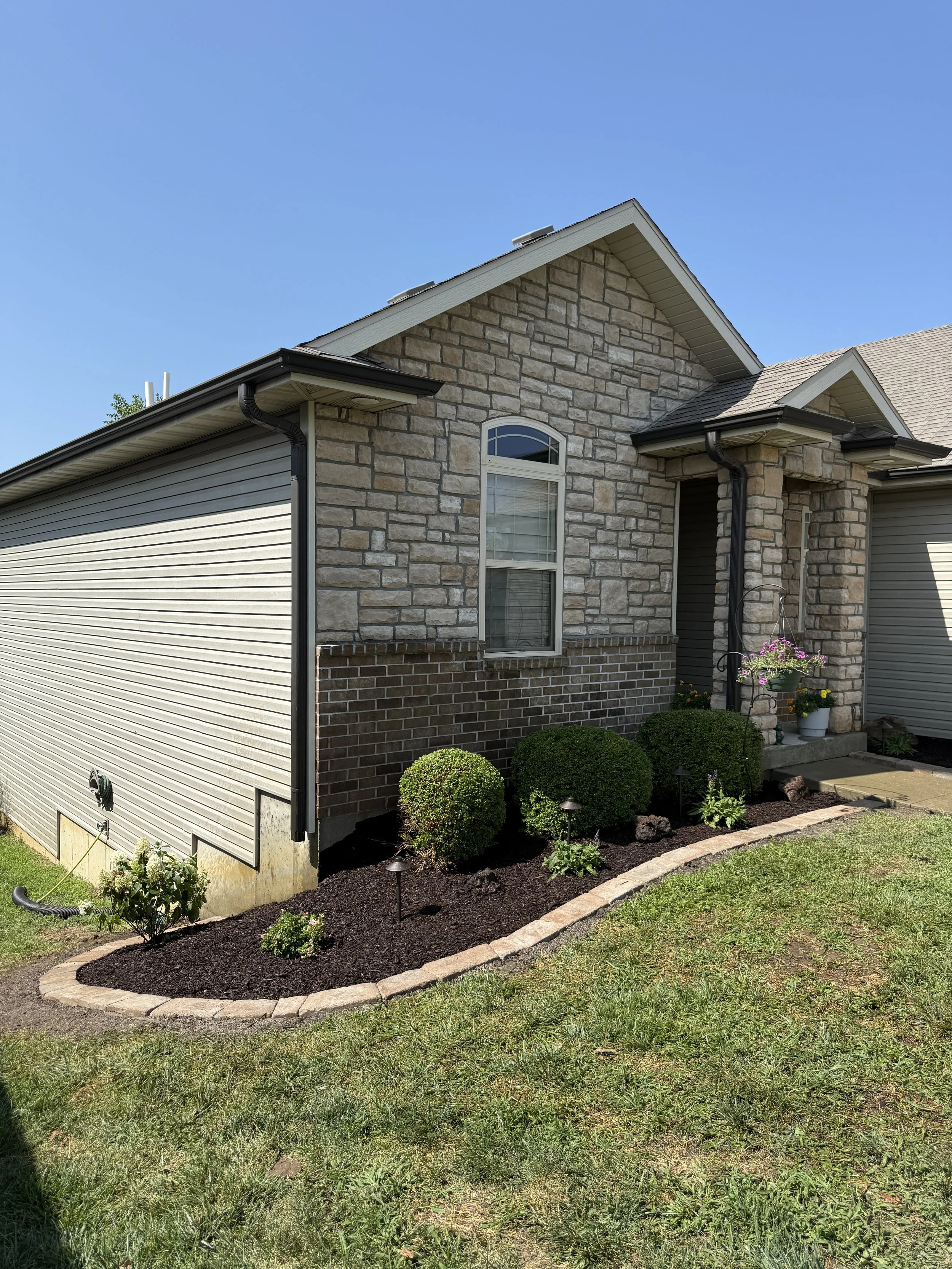 Stone-front home with a mulch bed, trimmed shrubs, and stone-edged landscaping