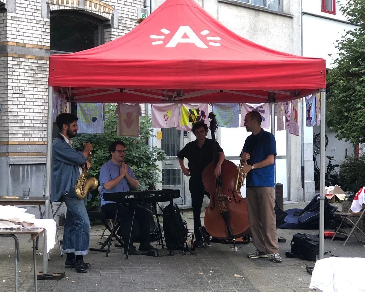Een groep muzikanten met instrumenten onder een rode tent tijdens een straatoptreden.