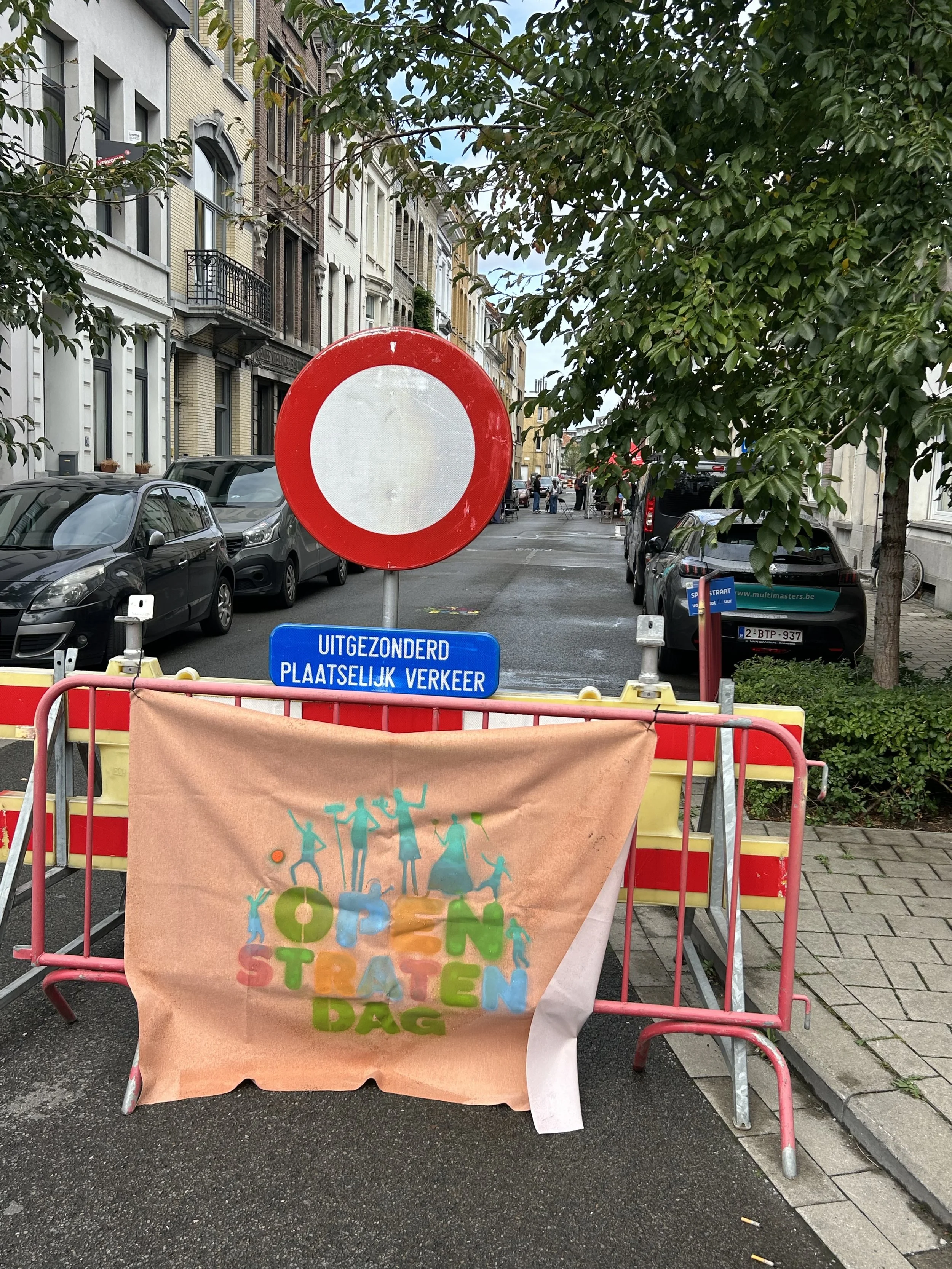 Een weg is afgesloten met een rood-wit verkeersbord en een geel-rode barrier met een doek dat 'Open Staten Dag' zegt, tijdens een evenement op een stadsstraat.