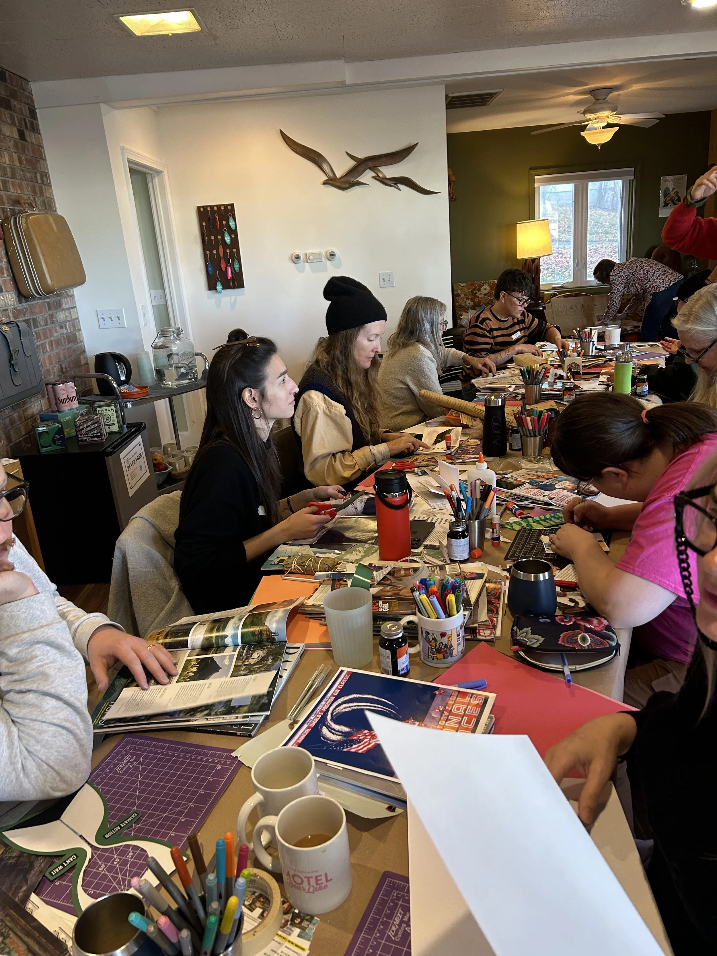 People gathered around a large table engaged in arts and crafts activities in a cozy room with a white wall decorated with metal bird sculptures and a green accent wall.
