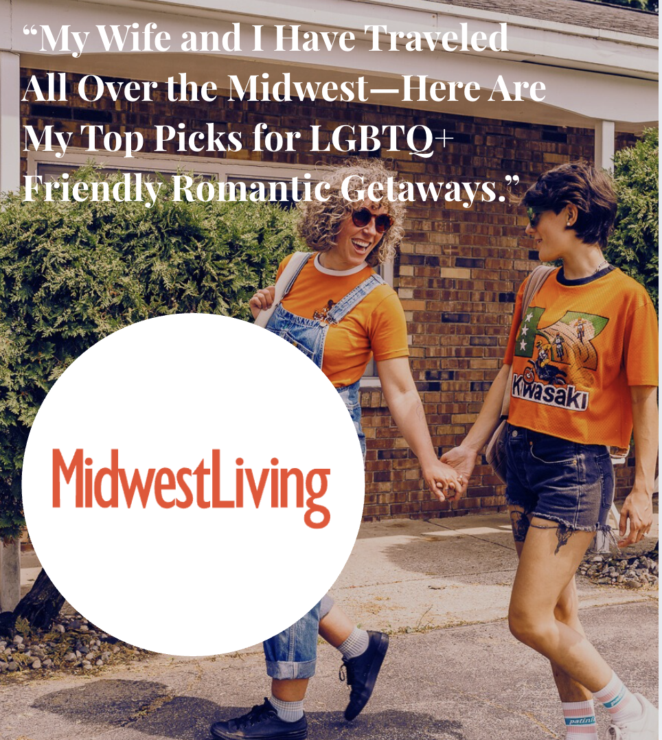Two women standing outside a brick house, smiling and talking to each other, surrounded by green bushes. One woman has curly gray hair and sunglasses, wearing an orange T-shirt and denim overalls. The other has short dark hair, sunglasses, and is wearing an orange Kawasaki T-shirt.