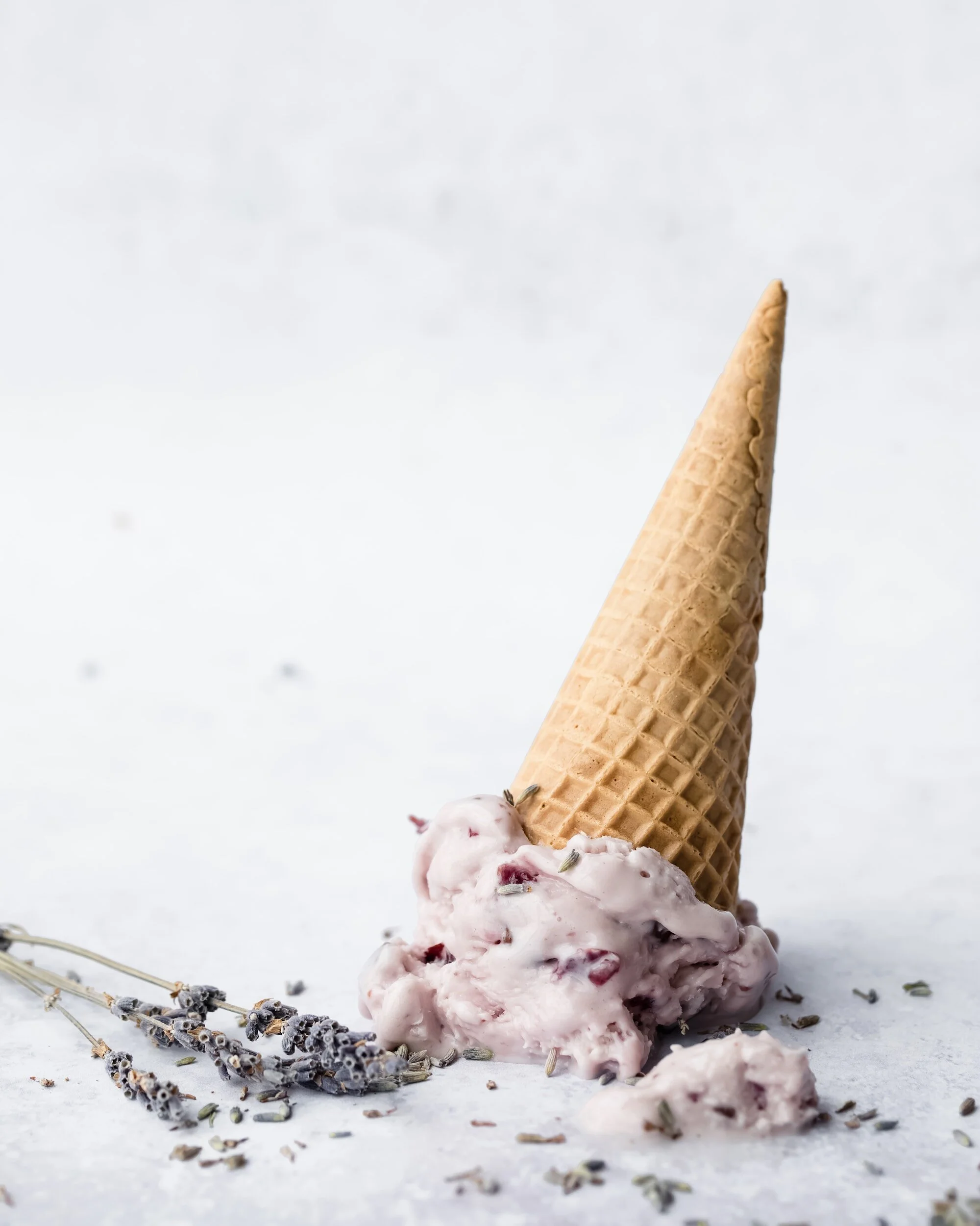 Ice cream cone upside down with the ice cream  on a grey surface with lavender petals around it