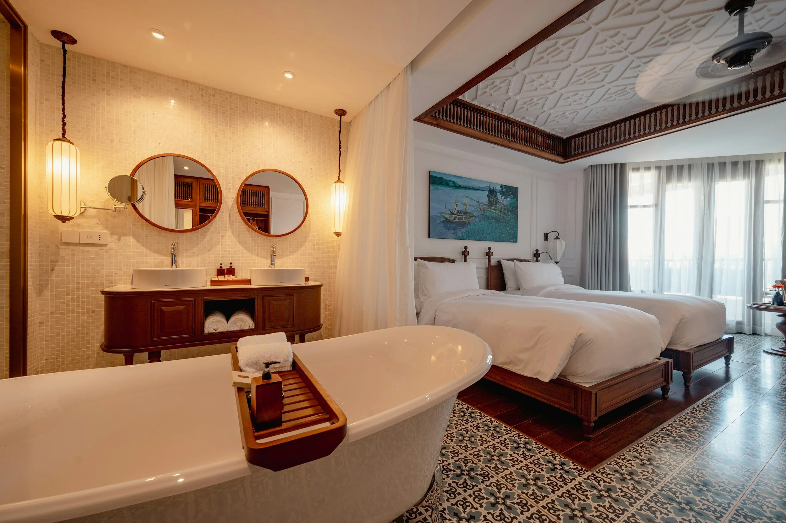 Luxury hotel room with two beds, a bathtub, and a bathroom vanity with two sinks and decorative mirrors.