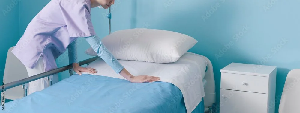 A healthcare professional making a bed in a hospital room.