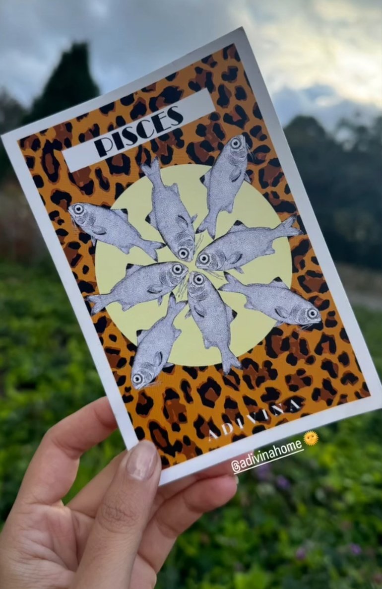 Une main tenant un magazine avec une couverture à motif léopard, représentant le signe astrologique Poissons avec plusieurs poissons en noir et blanc, et le mot "PISCES" écrit en haut.