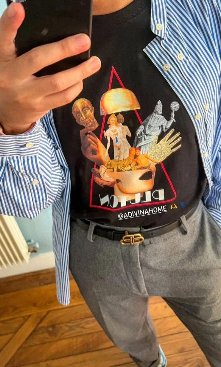 Un individu portant un t-shirt avec un collage d'images artistiques et un nom d'utilisateur Instagram, en train de se prendre en selfie.